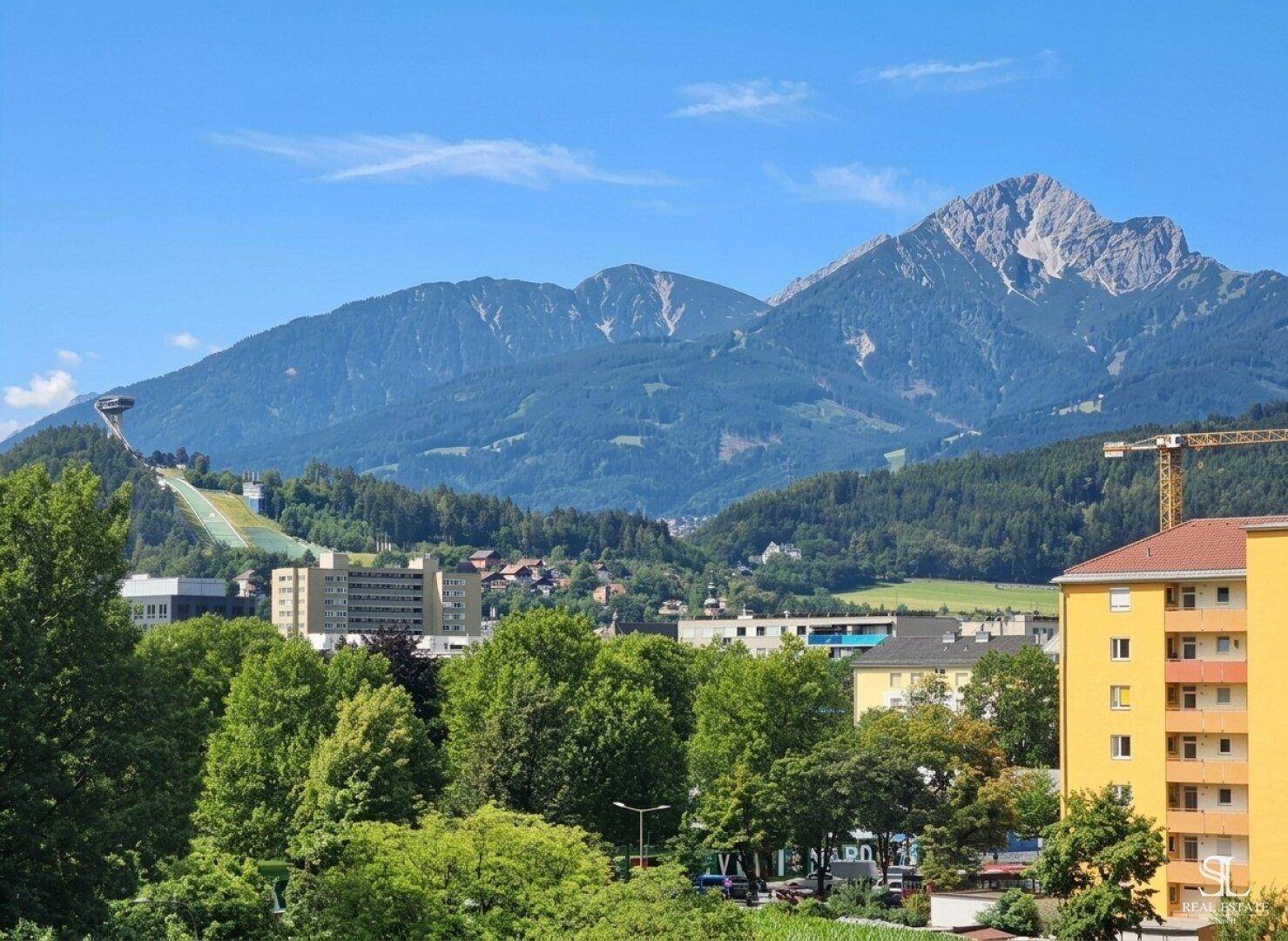 Panoramablick auf die Stadt und die umliegenden Berge unter blauem Himmel.