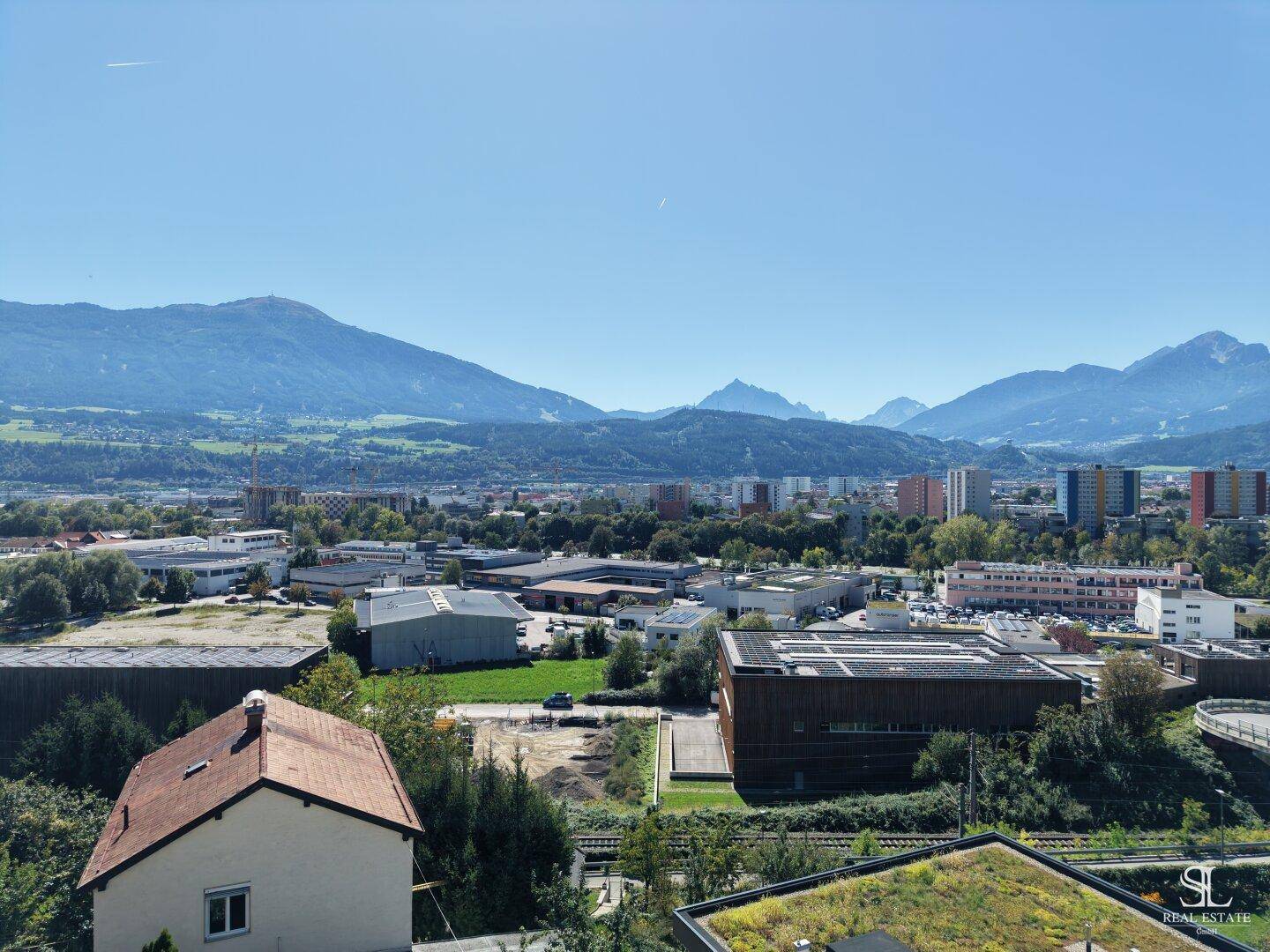 Weitläufiger Blick über die Stadt und die umliegende Berglandschaft unter blauem Himmel.