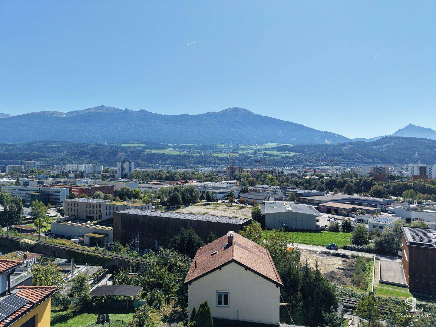 Panoramablick auf die Stadt mit ihren Gebäuden und der beeindruckenden Bergkulisse im Hintergrund.