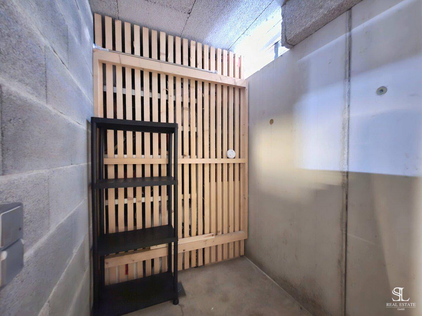 Abstellraum mit Betonwänden und einer Holzlamellentür, bietet zusätzlichen Stauraum.