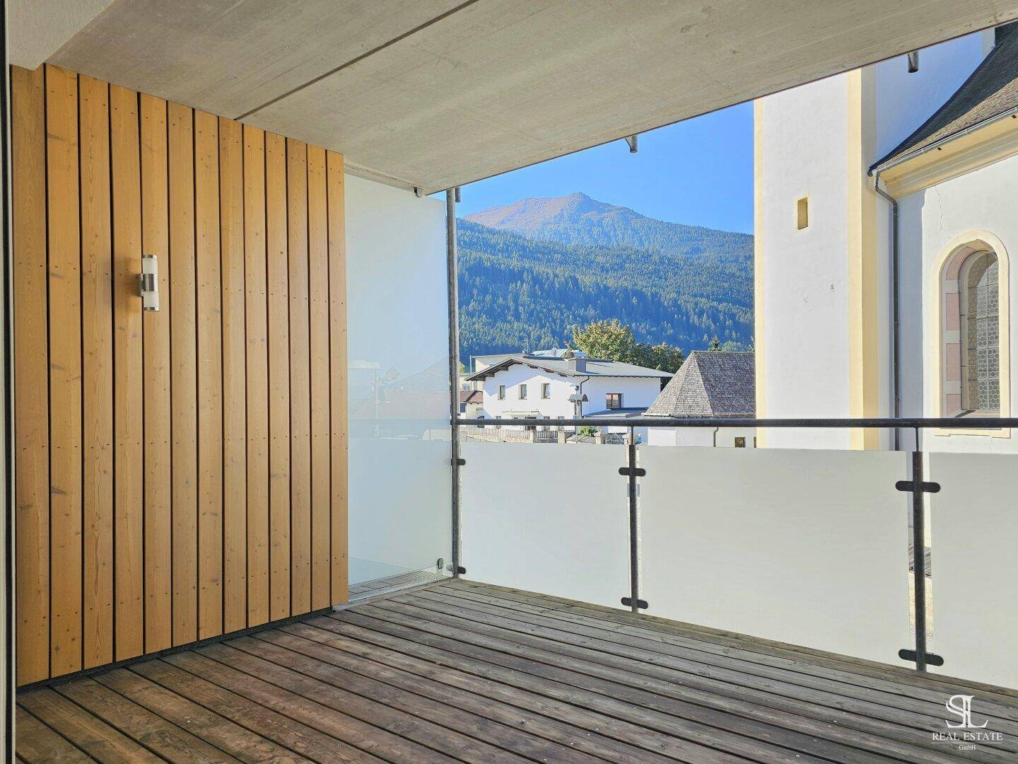 Geräumiger Balkon mit Holzboden und Glasgeländer, bietet einen weiten Blick auf die Berge.