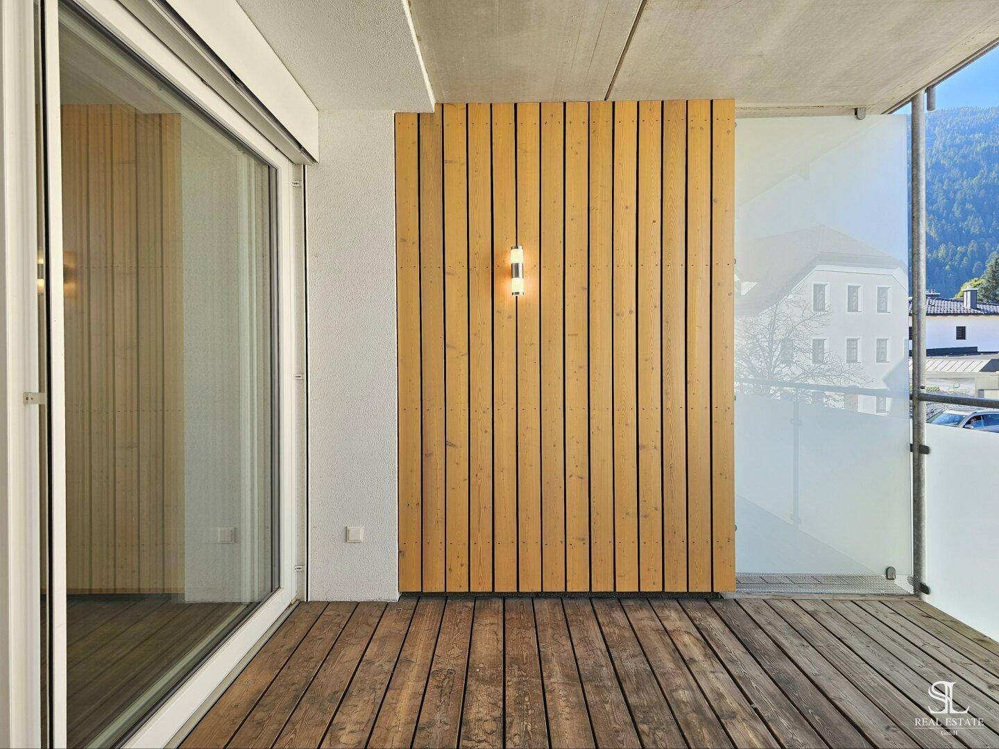 Balkon mit Holzboden und Holzverkleidung, zugänglich durch eine große Glasschiebetür.