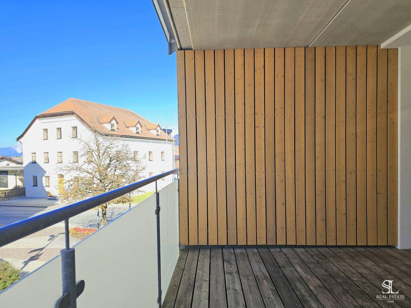 Balkon mit Holzboden und Blick auf ein historisches Gebäude sowie die umliegende Berglandschaft.