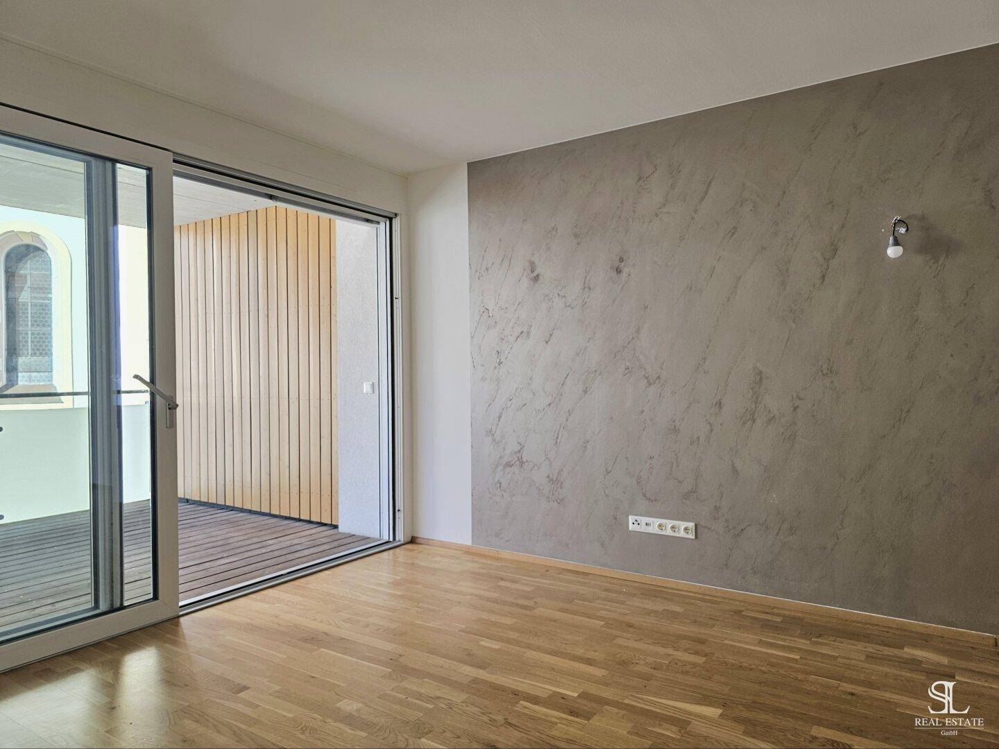 Zimmer mit Holzboden und Akzentwand, mit direktem Zugang zu einem sonnigen Balkon.