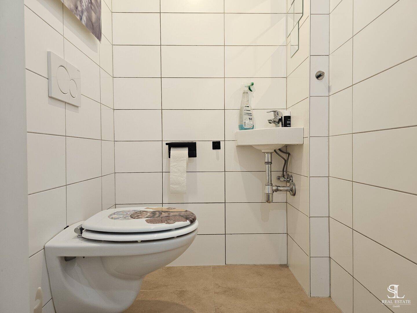 Kleines Gäste-WC mit wandhängender Toilette, kleinem Waschbecken und weißen Fliesen.