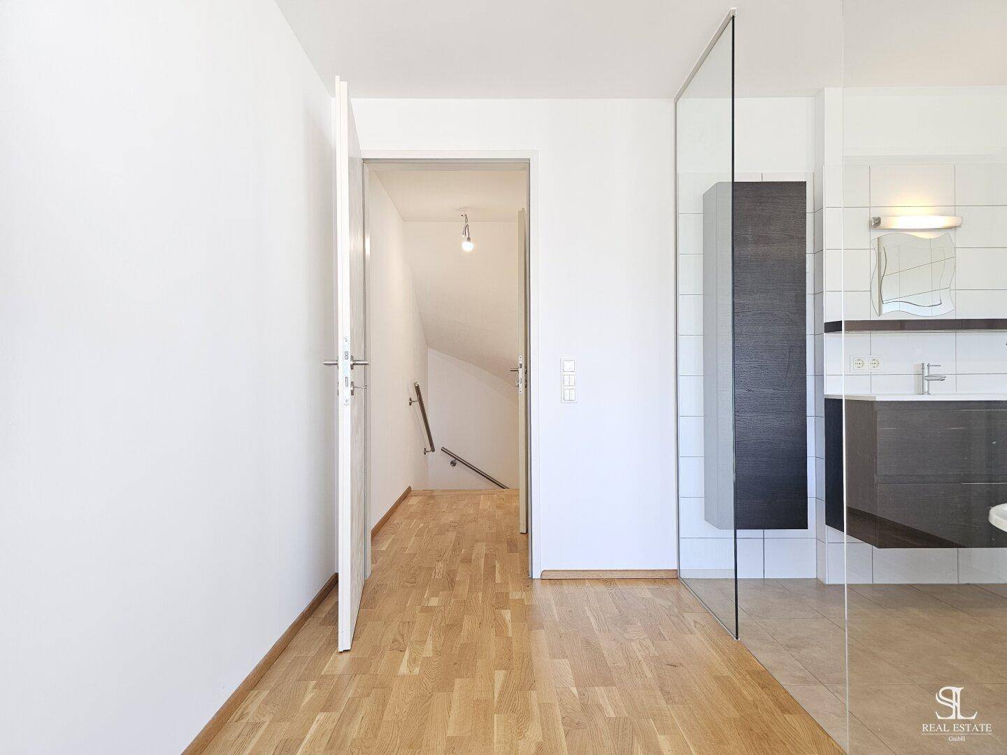 Heller Flur mit Holzboden, der zu einer Treppe führt und einen Blick auf das Badezimmer bietet.