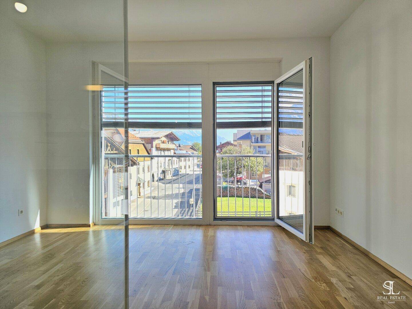 Heller Raum mit Holzboden und großen Fenstern, die einen weiten Blick auf die Umgebung ermöglichen.
