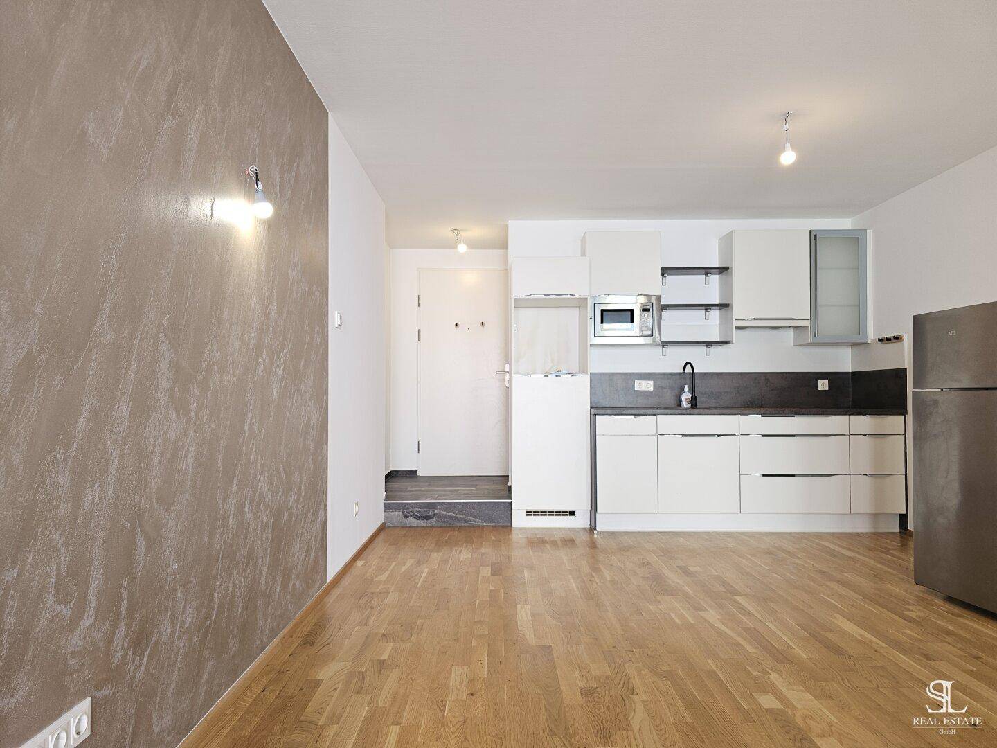 Offener Wohnbereich mit Küchenzeile, Holzboden und modernem Kühlschrank.