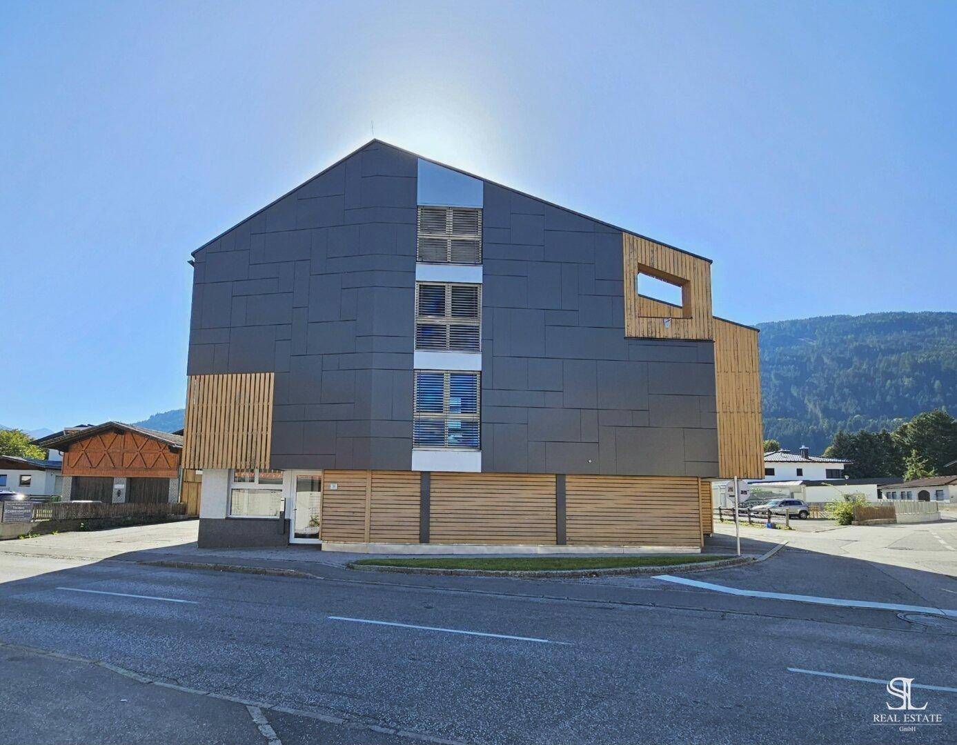 Moderne Architektur mit dunkler Fassadenverkleidung und Holzelementen vor einer Bergkulisse.