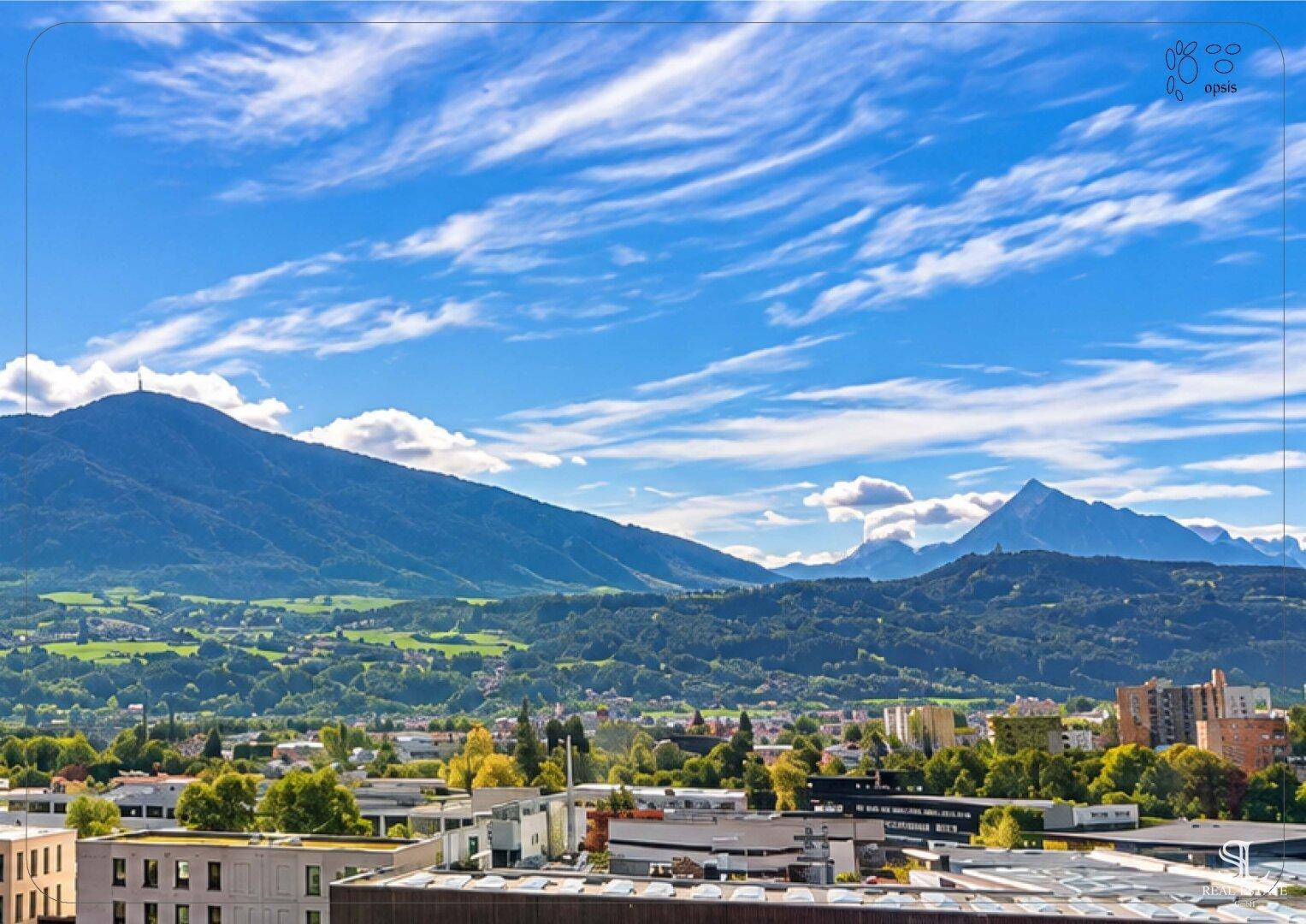 Weitläufiger Blick über die Stadt und die umliegende Berglandschaft unter blauem Himmel.