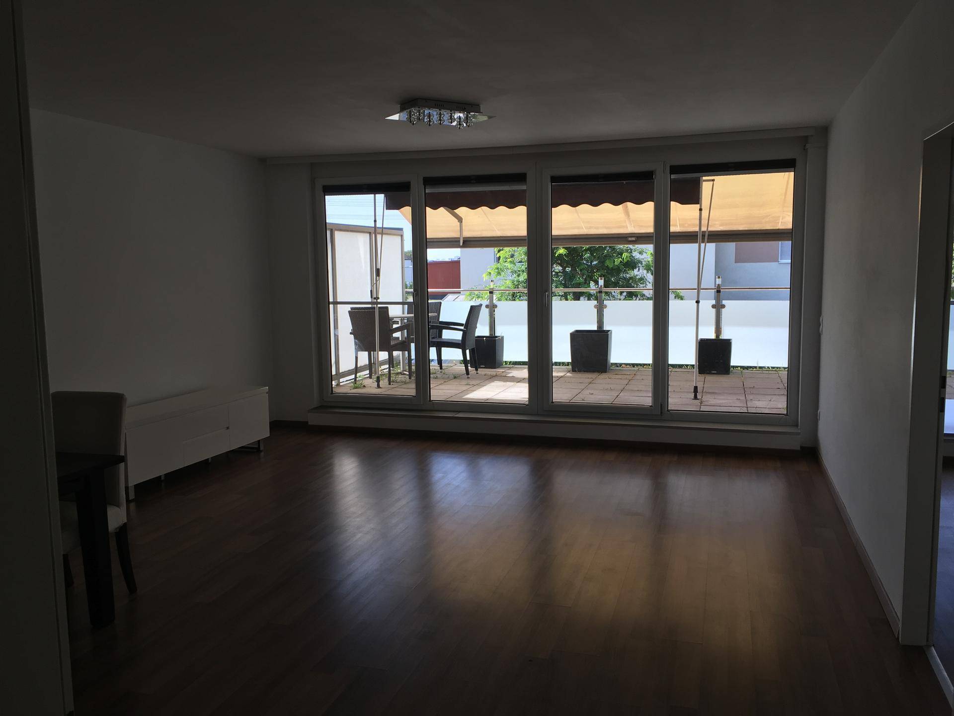 Geräumiges Wohnzimmer mit Holzboden und großen Fenstern mit Blick auf die Terrasse.
