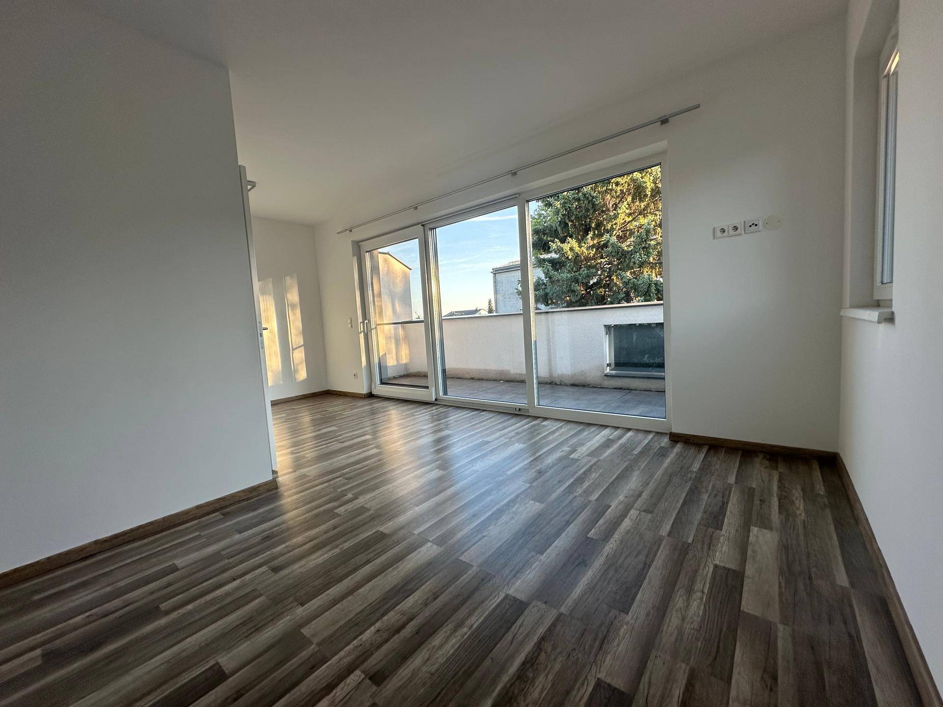 Heller Wohnraum mit Laminatboden und breiter Schiebetür zum Balkon.