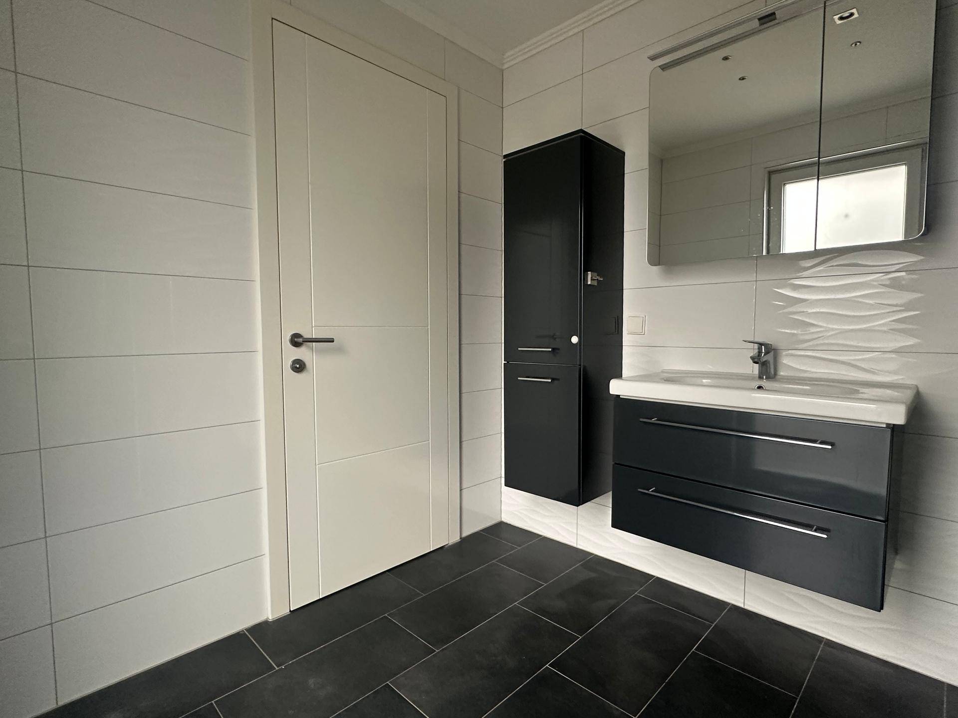 Modernes Badezimmer mit Waschbeckenunterschrank, Spiegelschrank und weißer Tür.