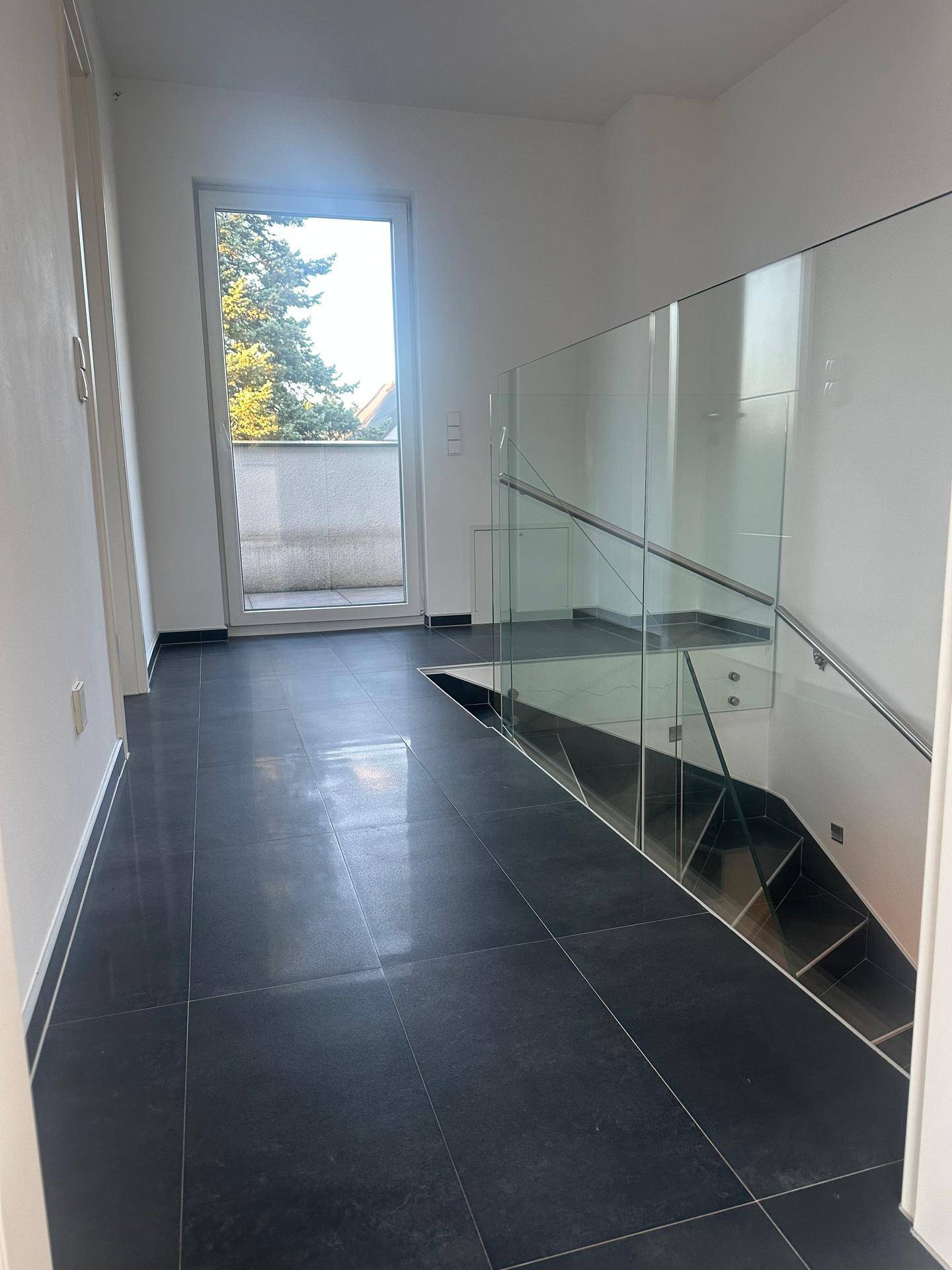 Heller Flur im Obergeschoss mit Glasgeländer und Zugang zu einem französischen Balkon.