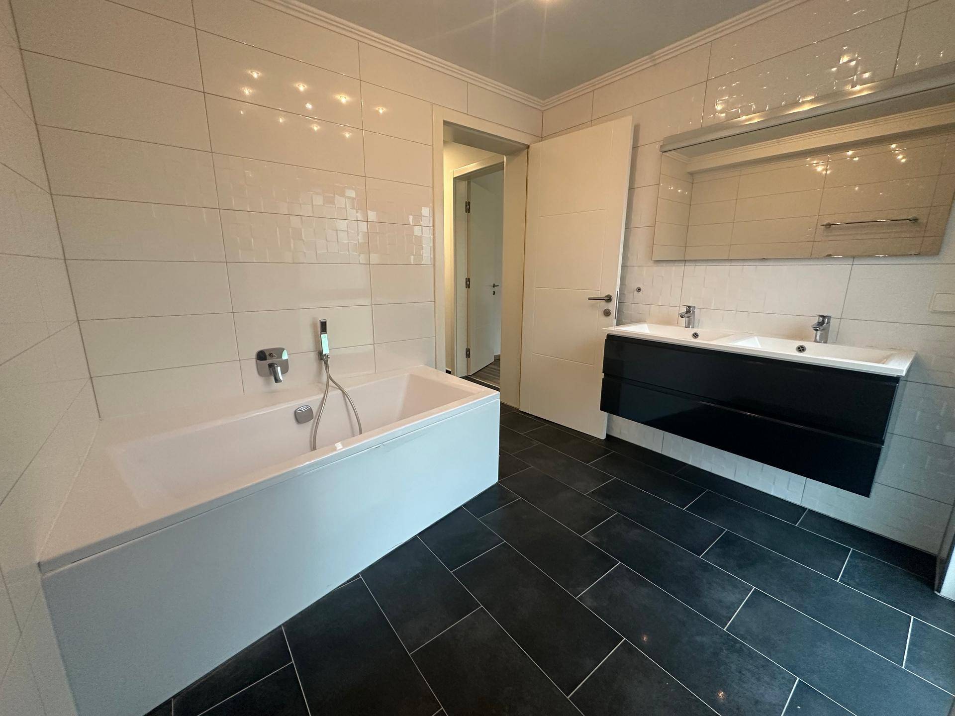 Geräumiges Badezimmer mit Badewanne, Doppelwaschbecken und dunklem Fliesenboden.