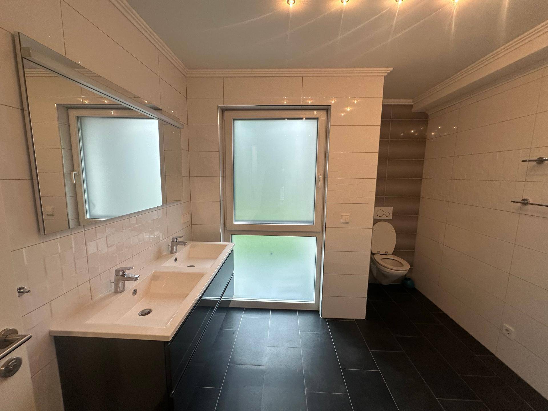 Helles Badezimmer mit Doppelwaschbecken, großem Spiegel und Fenster.