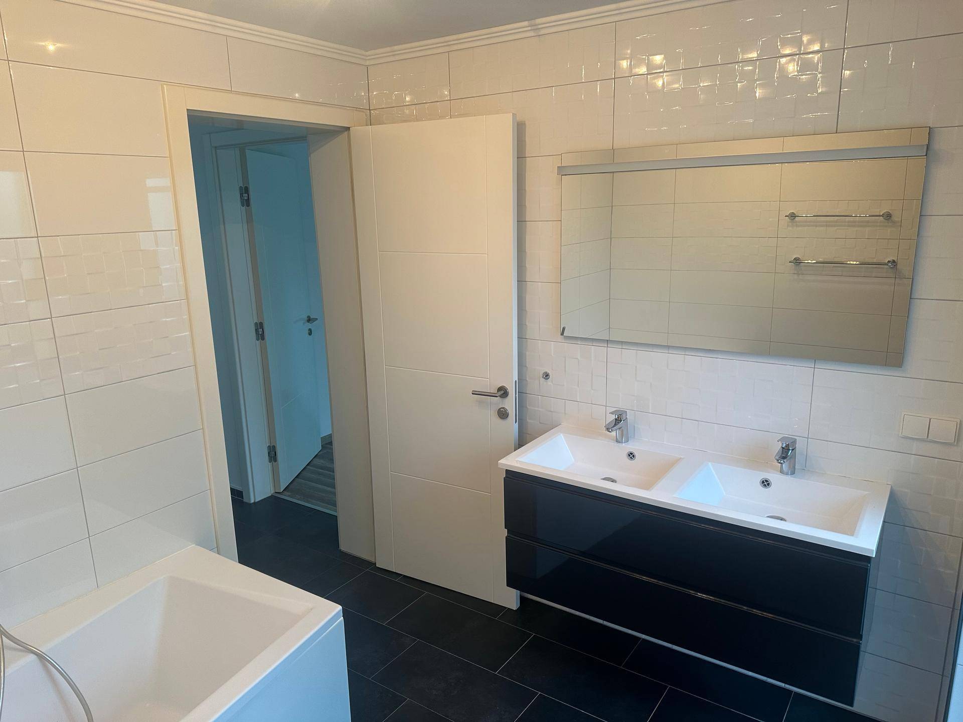 Modernes Badezimmer mit Doppelwaschbecken, Badewanne und weißen Wandfliesen.