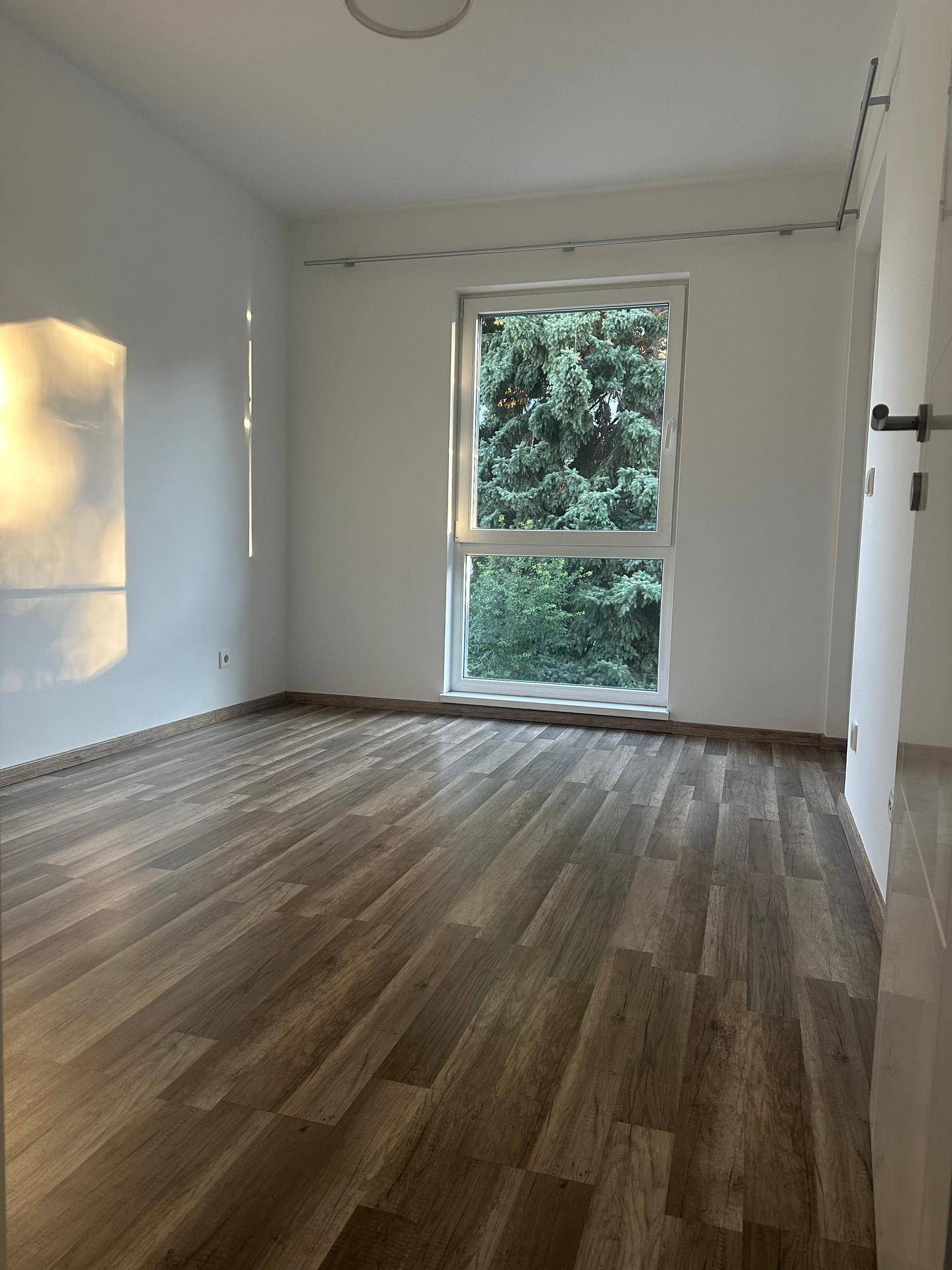 Geräumiges Schlafzimmer mit Laminatboden und großem Fenster mit Baumblick.