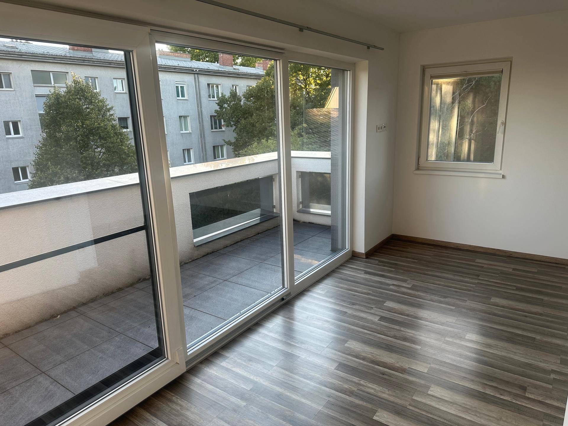 Geräumiger Raum mit Laminatboden und großem Balkonfenster, bietet viel Licht.