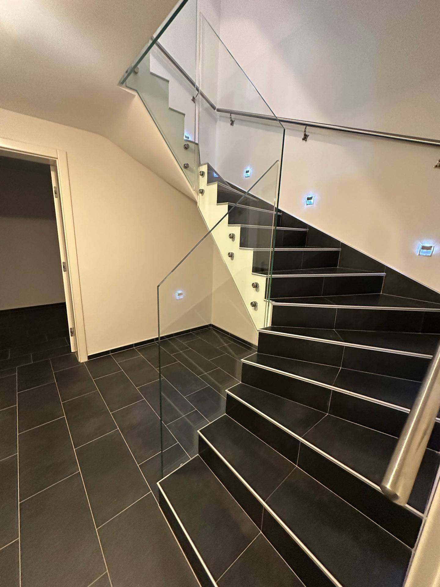 Moderne Treppe mit Glasgeländer und dunklen Fliesen im Eingangsbereich.