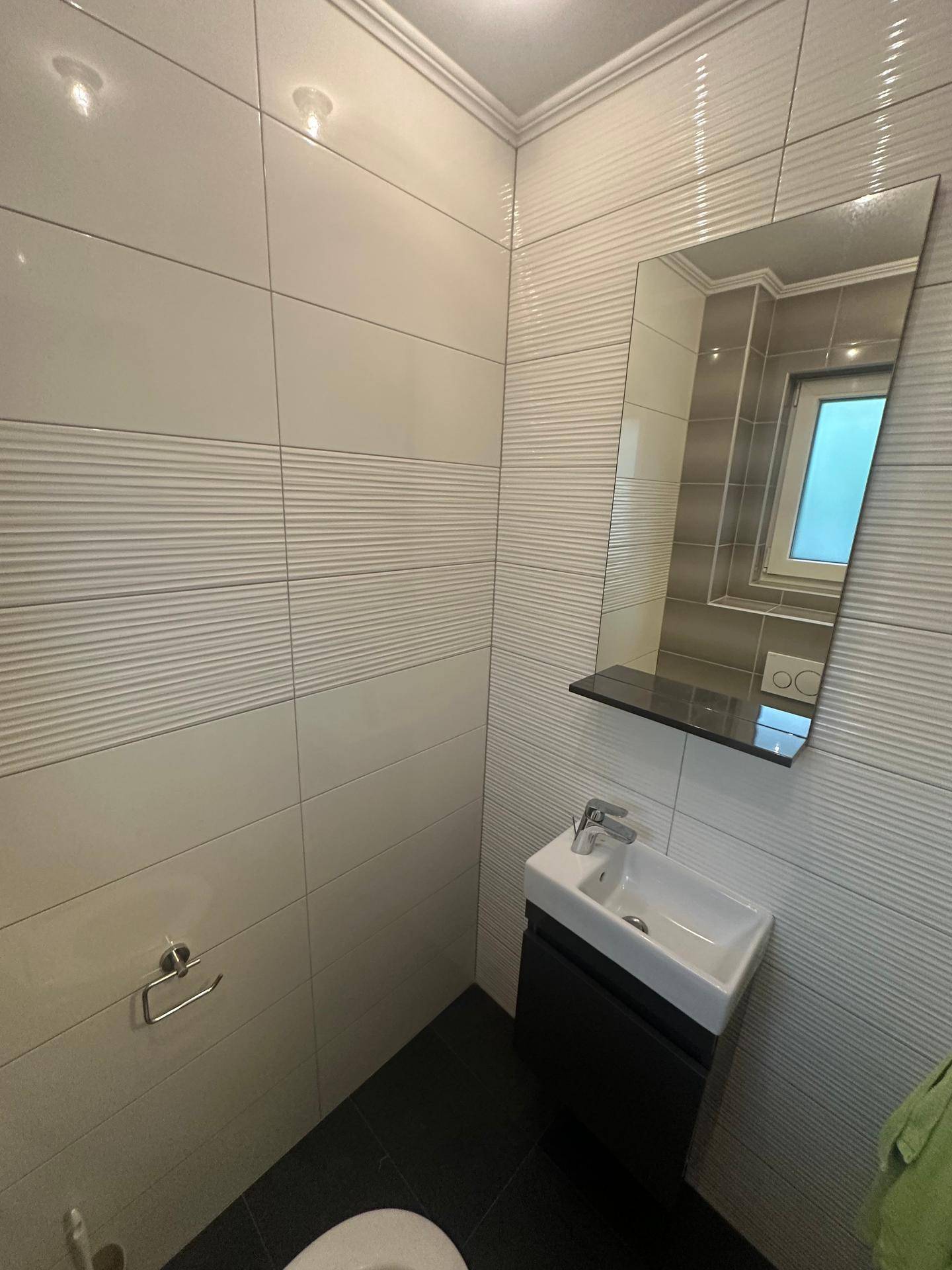 Modernes Gäste-WC mit kleinem Waschbecken, Spiegel und strukturierten Wandfliesen.