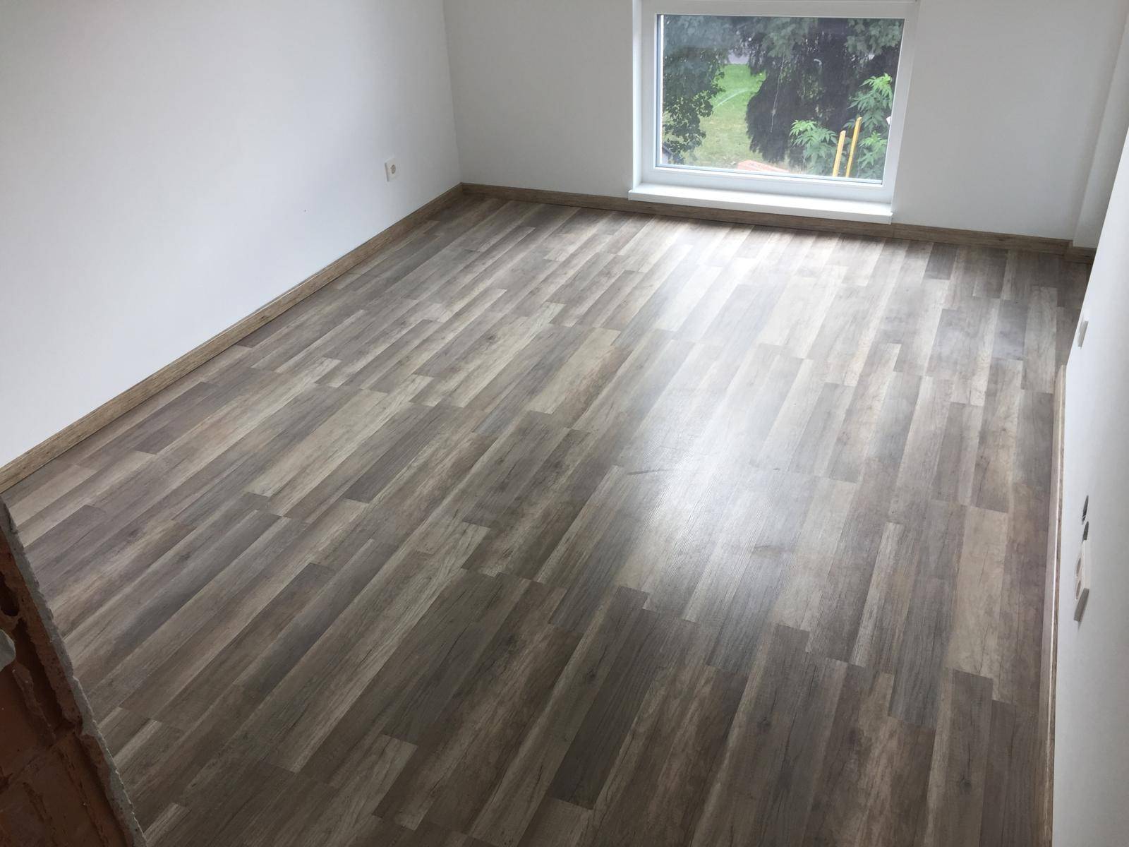 Helles Schlafzimmer mit modernem Laminatboden und Fenster mit Grünblick.