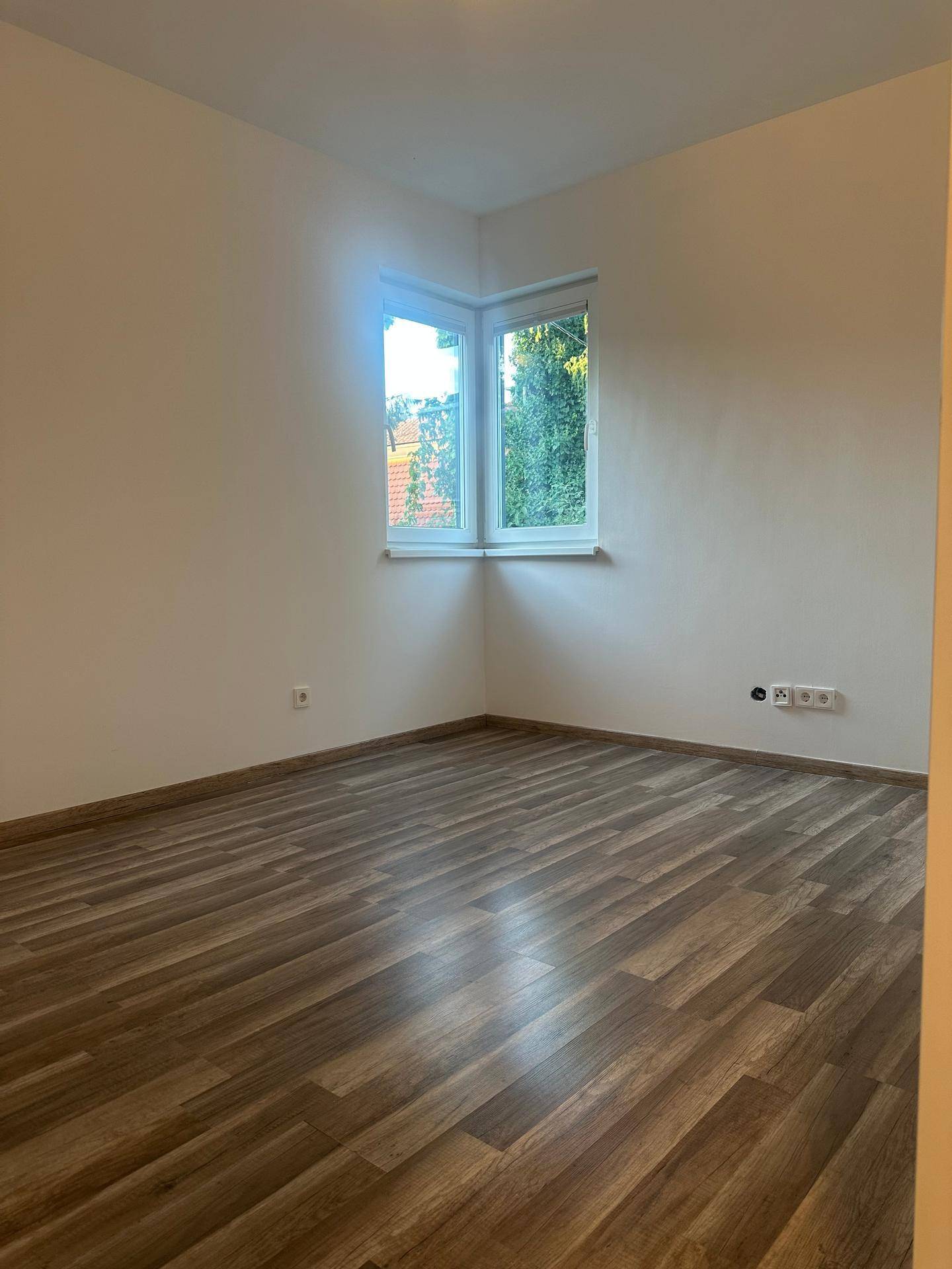 Helles Schlafzimmer mit Laminatboden und Eckfenster mit Blick ins Grüne.