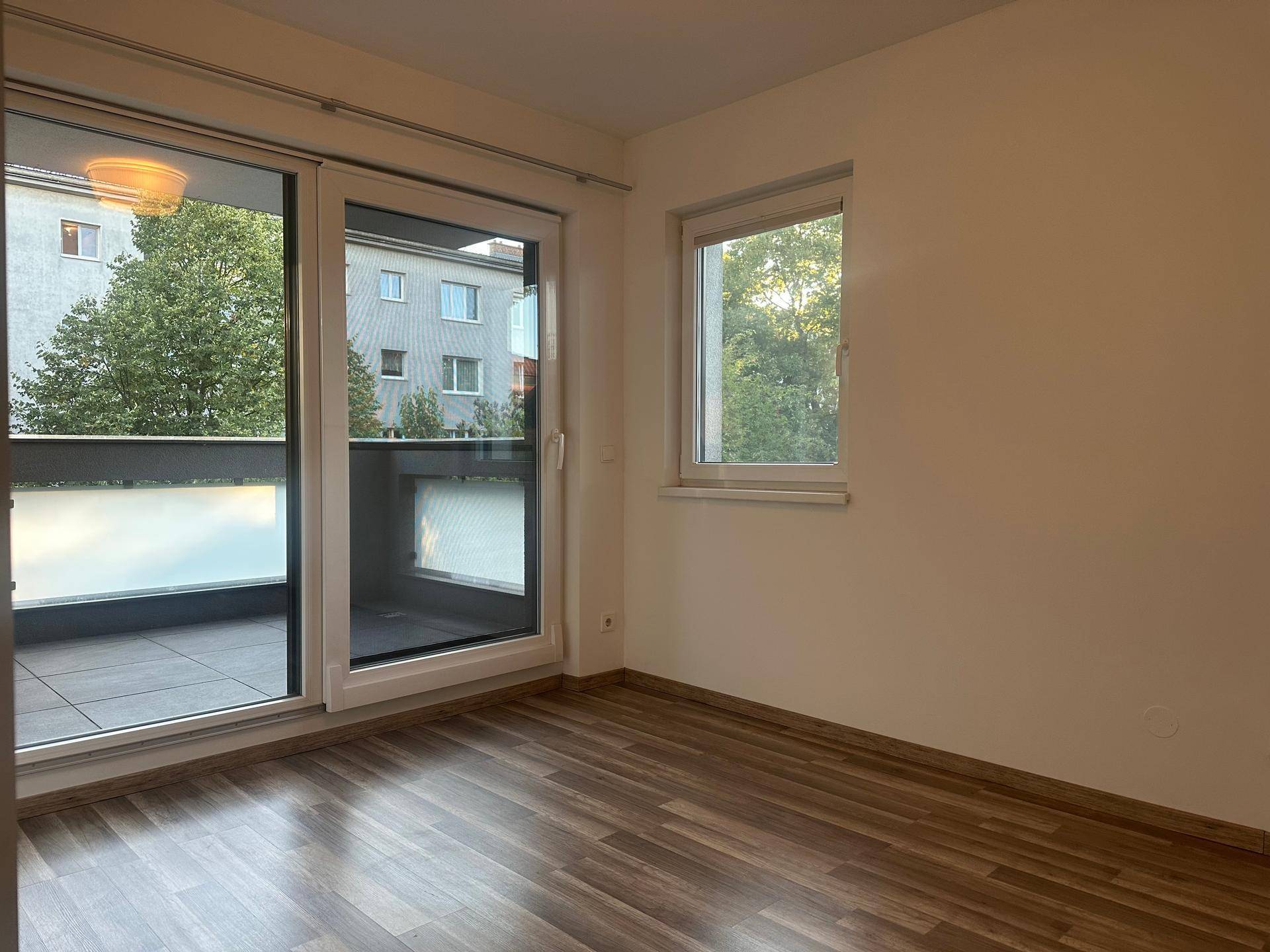 Schlafzimmer mit Laminatboden, großem Fenster und Zugang zum Balkon.