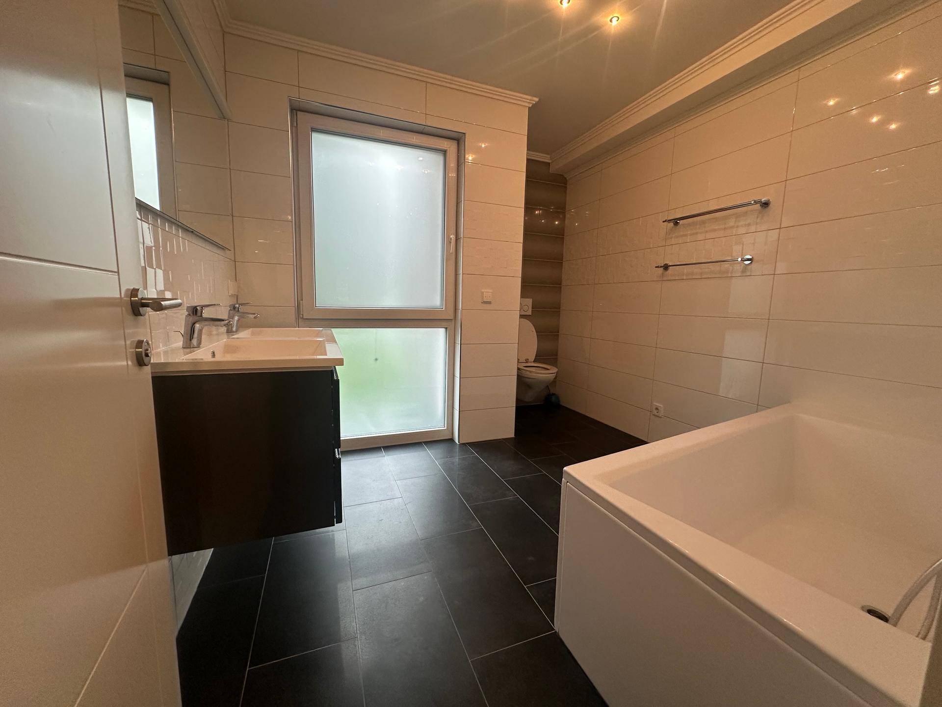 Modernes Badezimmer mit Badewanne, Doppelwaschbecken und Fenster mit Milchglas.