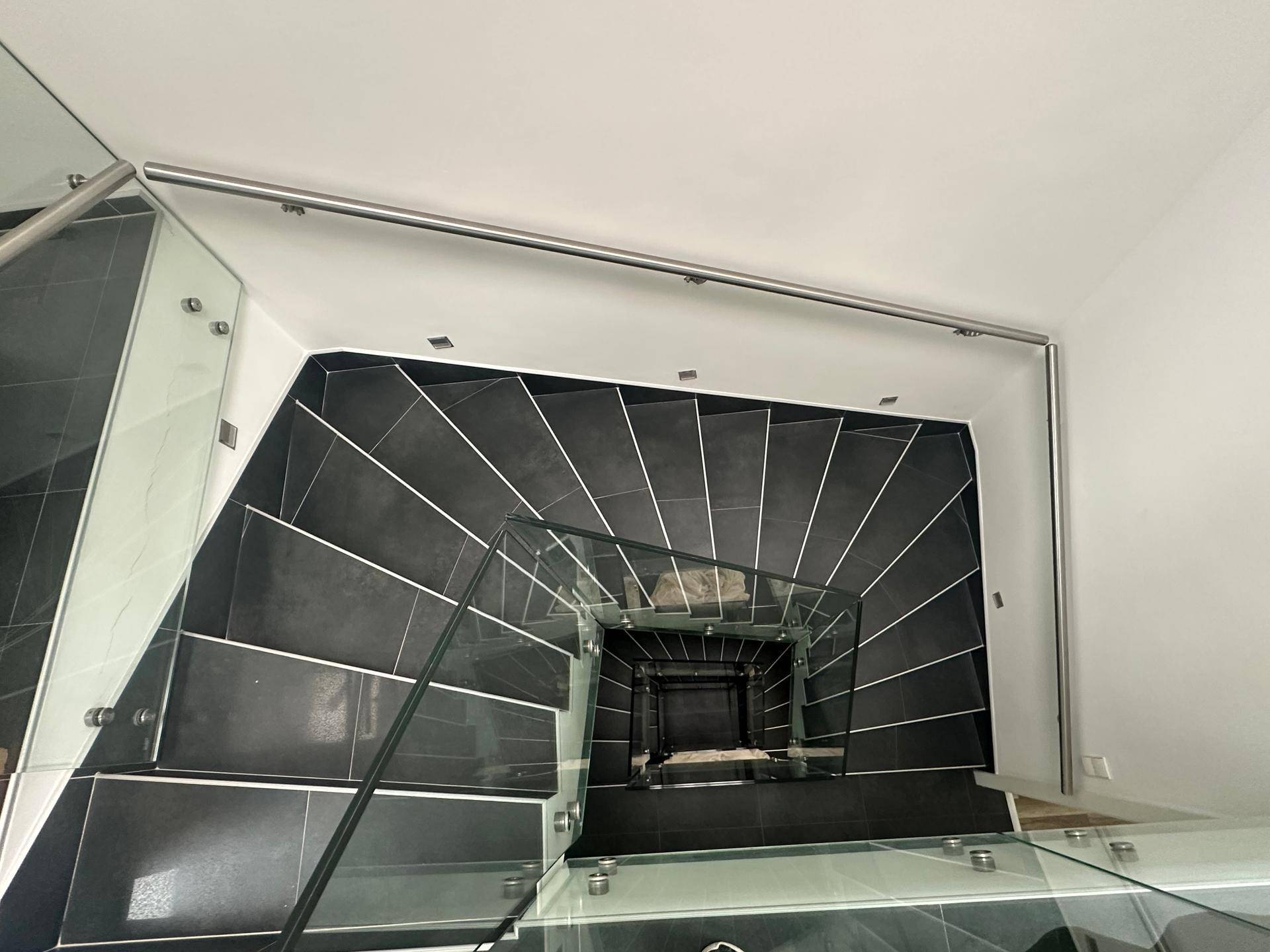 Blick von oben auf das moderne Treppenhaus mit Glasgeländer und dunklen Stufen.