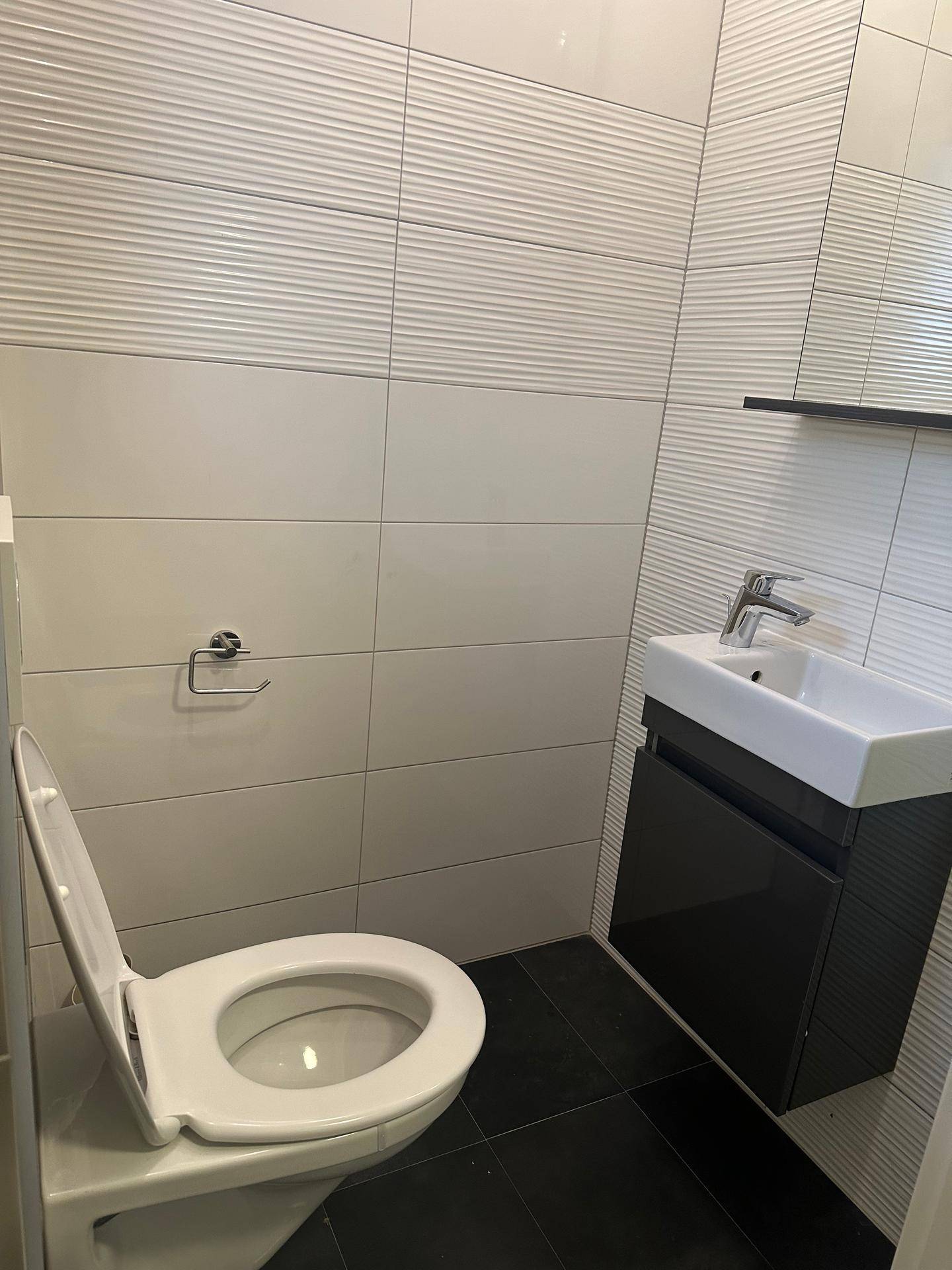 Modernes Gäste-WC mit wandhängendem WC, kleinem Waschbecken und strukturierten Fliesen.