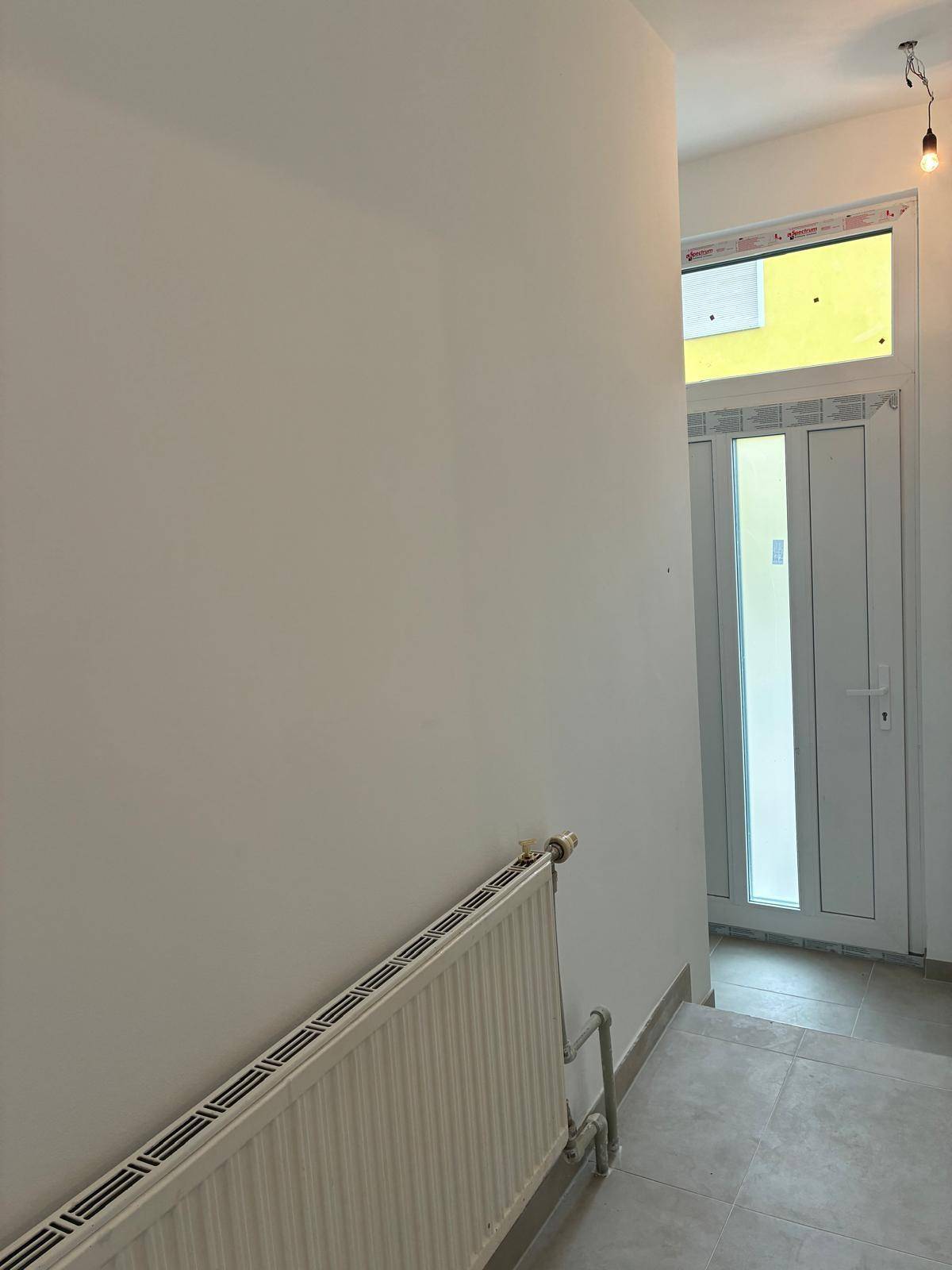 Heller Eingangsbereich mit Fliesenboden, Heizkörper und einer modernen Eingangstür mit Glaseinsätzen.