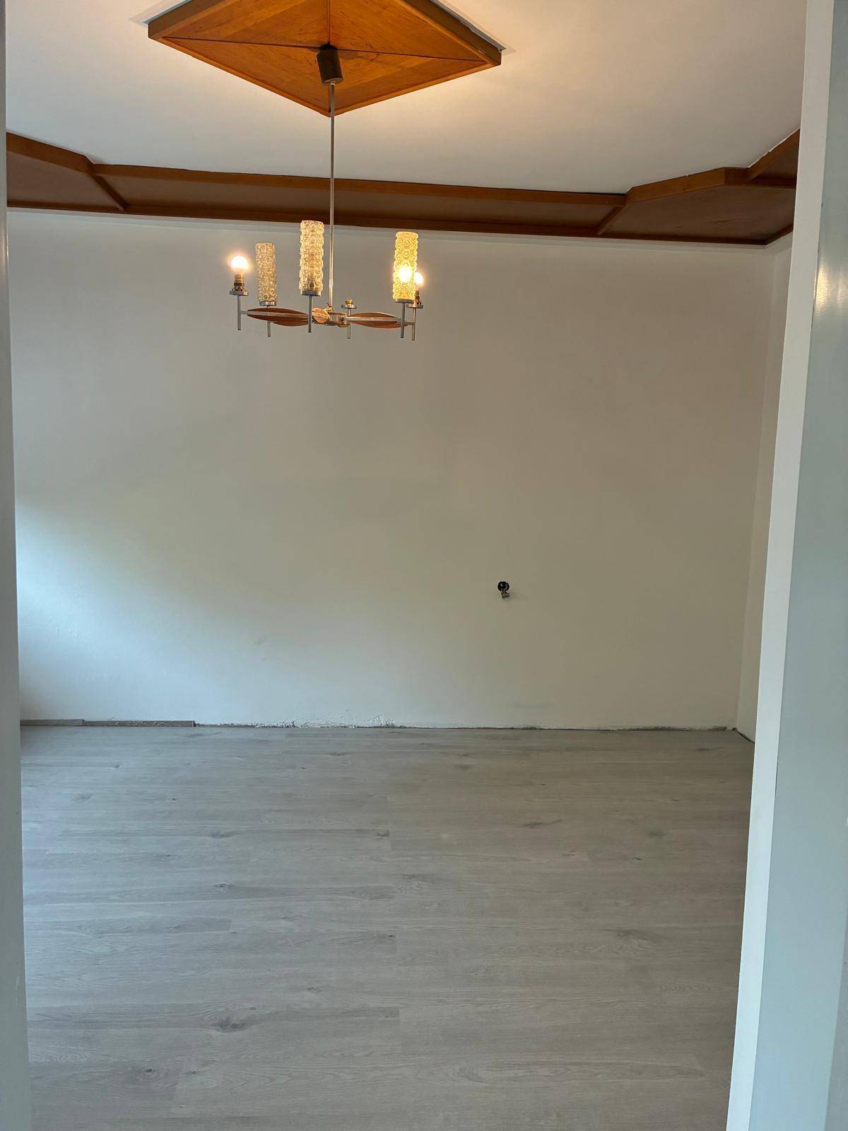 Geräumiges Zimmer mit hellem Laminatboden und einer auffälligen Holzdeckenverkleidung mit Leuchte.
