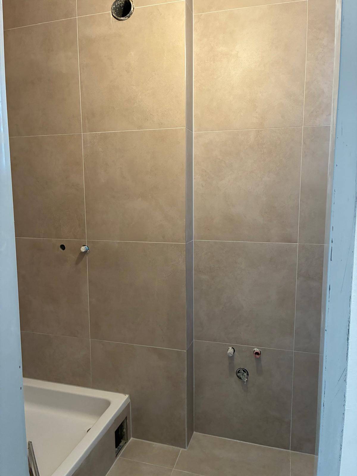 Unfertiges Badezimmer mit beigen Fliesen an Wänden und Boden, sowie einer sichtbaren Badewanne.