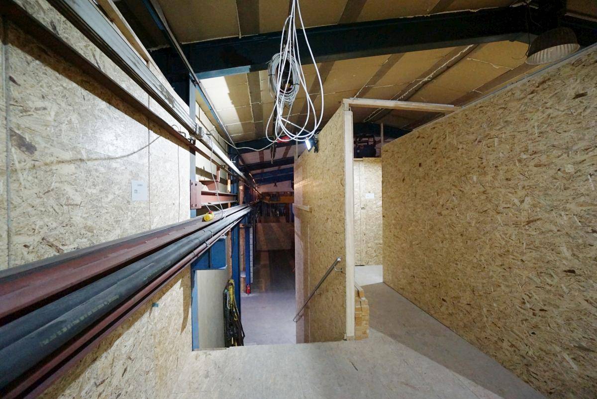 Industrieller Innenraum mit sichtbaren Trägern, Kabeln und OSB-Plattenwänden, der einen Abstieg zeigt.