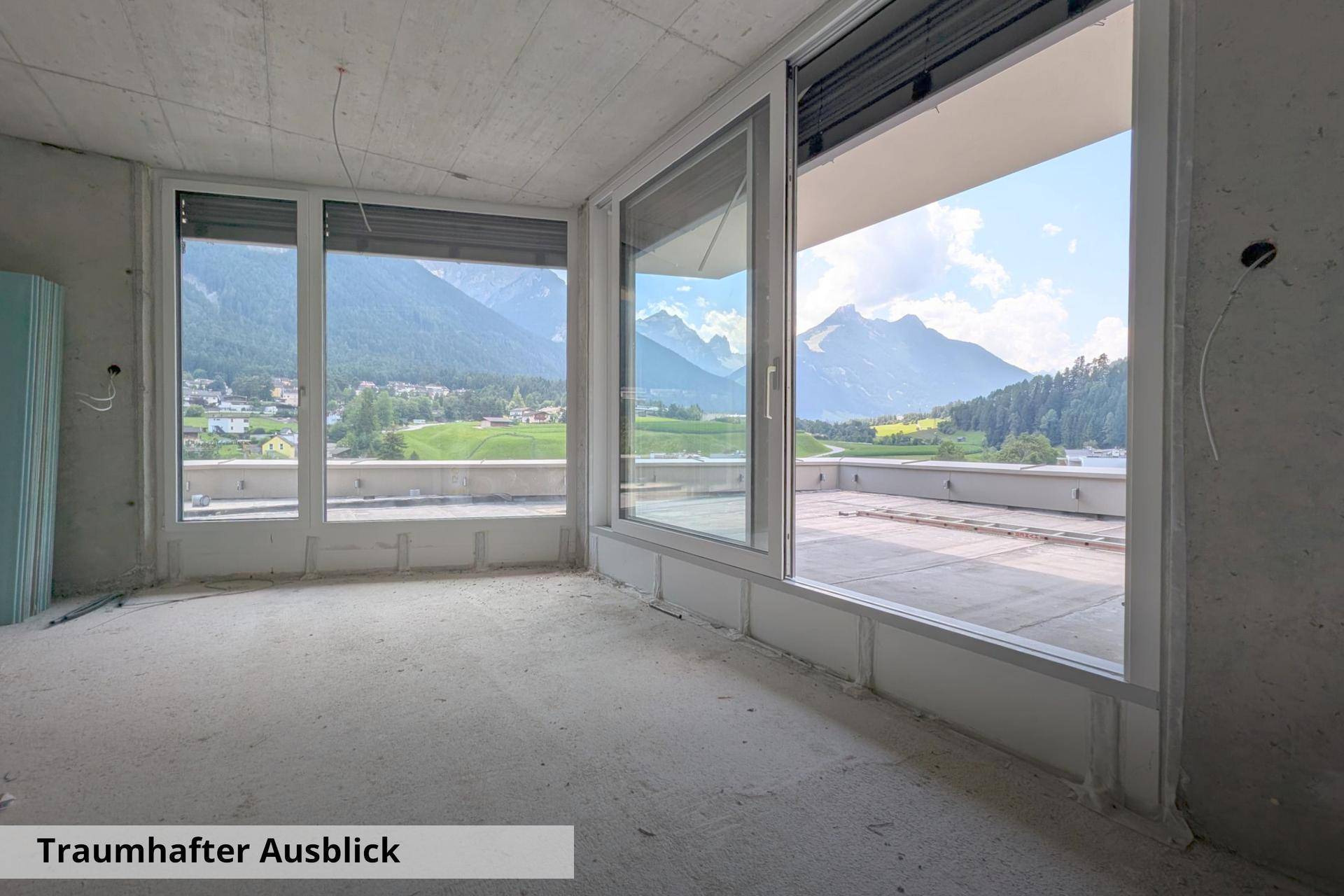 Heller Innenraum im Rohbau mit raumhohen Fenstern und einem atemberaubenden Blick auf die Berge.