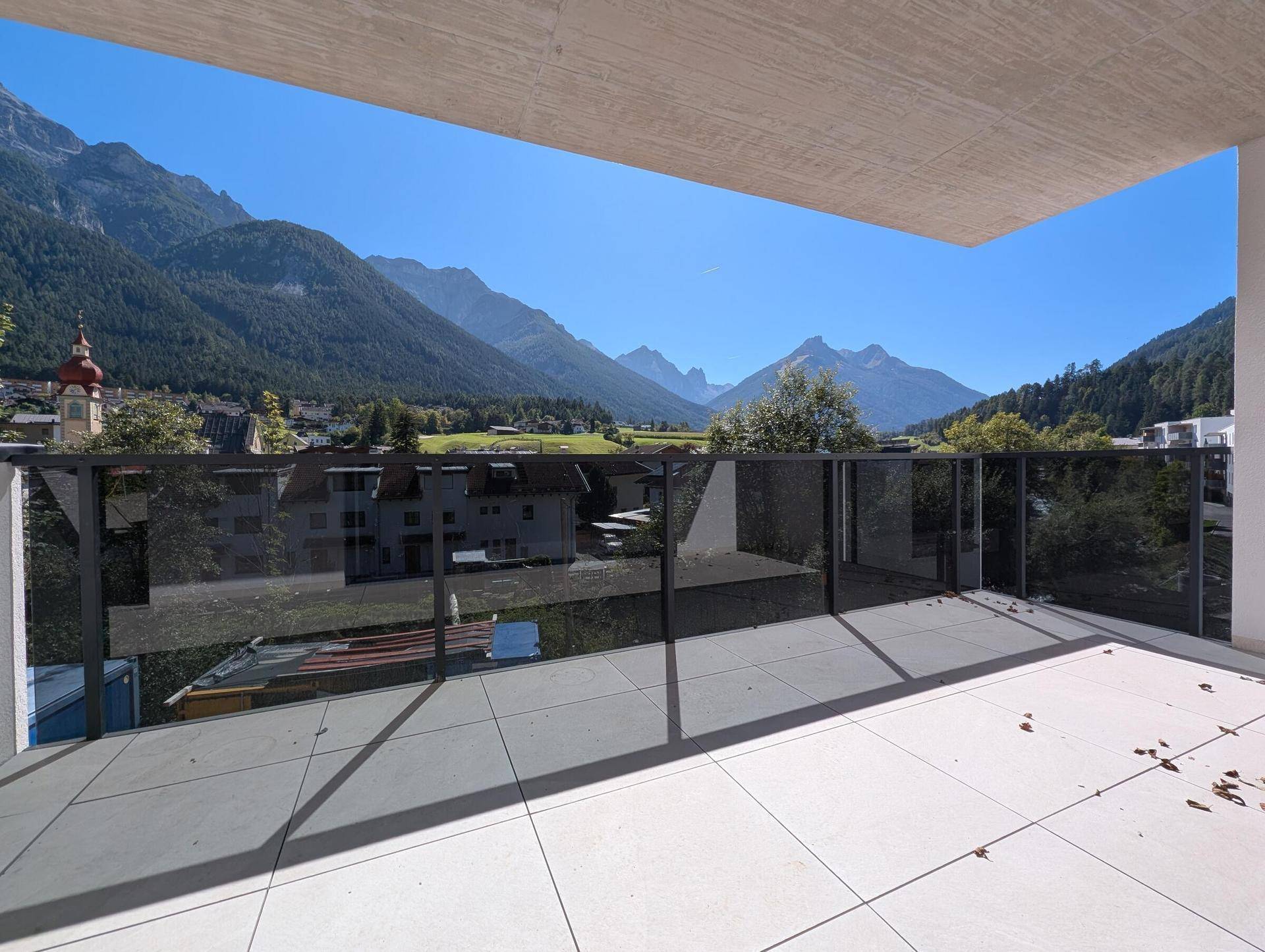 Geräumiger Balkon mit Glasgeländer und weitem Blick auf die umliegende Bergwelt.