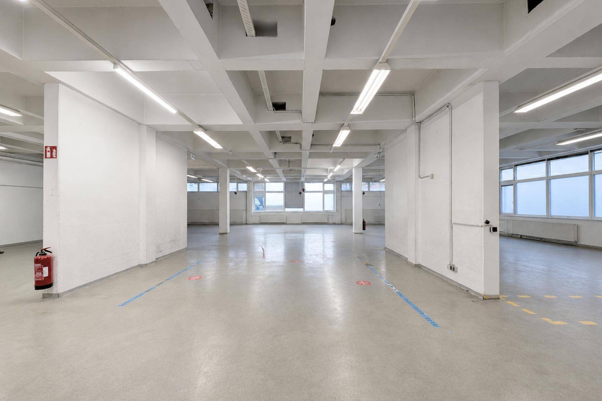 Helle Industriehalle mit Betonboden, hohen Decken und vielen Fenstern, ideal für gewerbliche Zwecke.