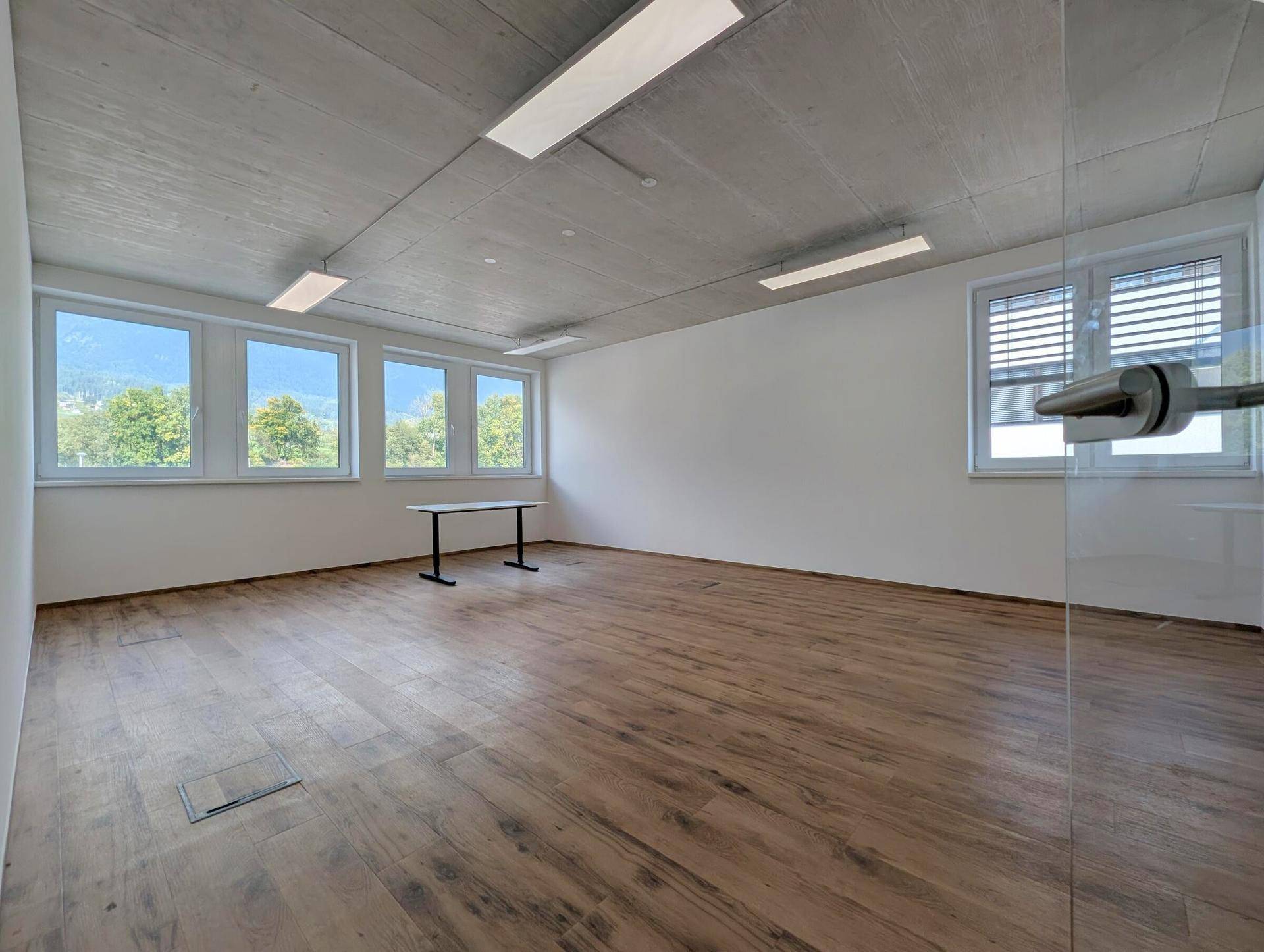 Leerer Büroraum mit Holzboden, großen Fenstern und viel Tageslicht, bereit zur individuellen Einrichtung.