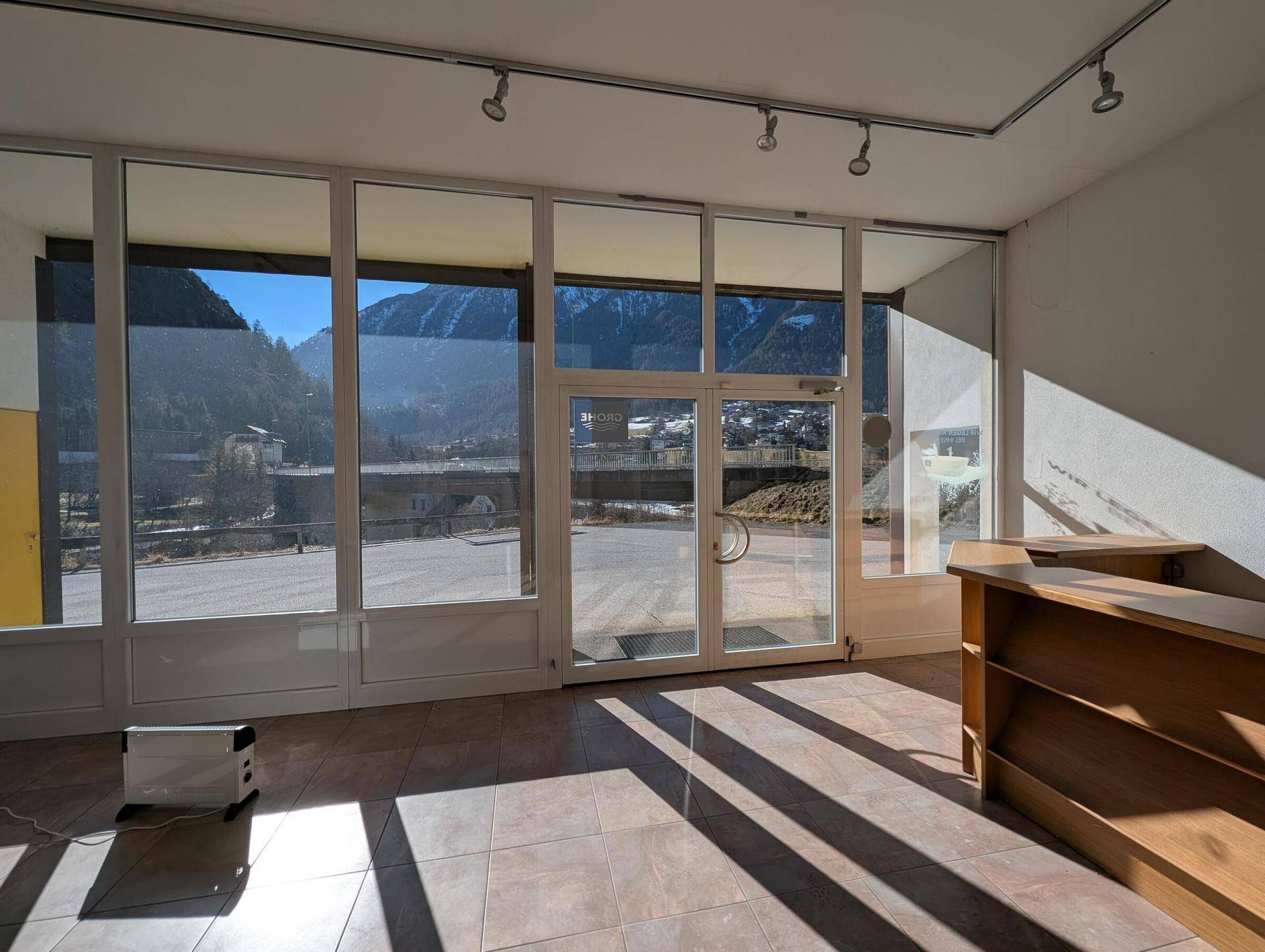 Heller Empfangsbereich mit großen Glasfronten, Fliesenboden und Bergblick, ideal für Kundenempfang.