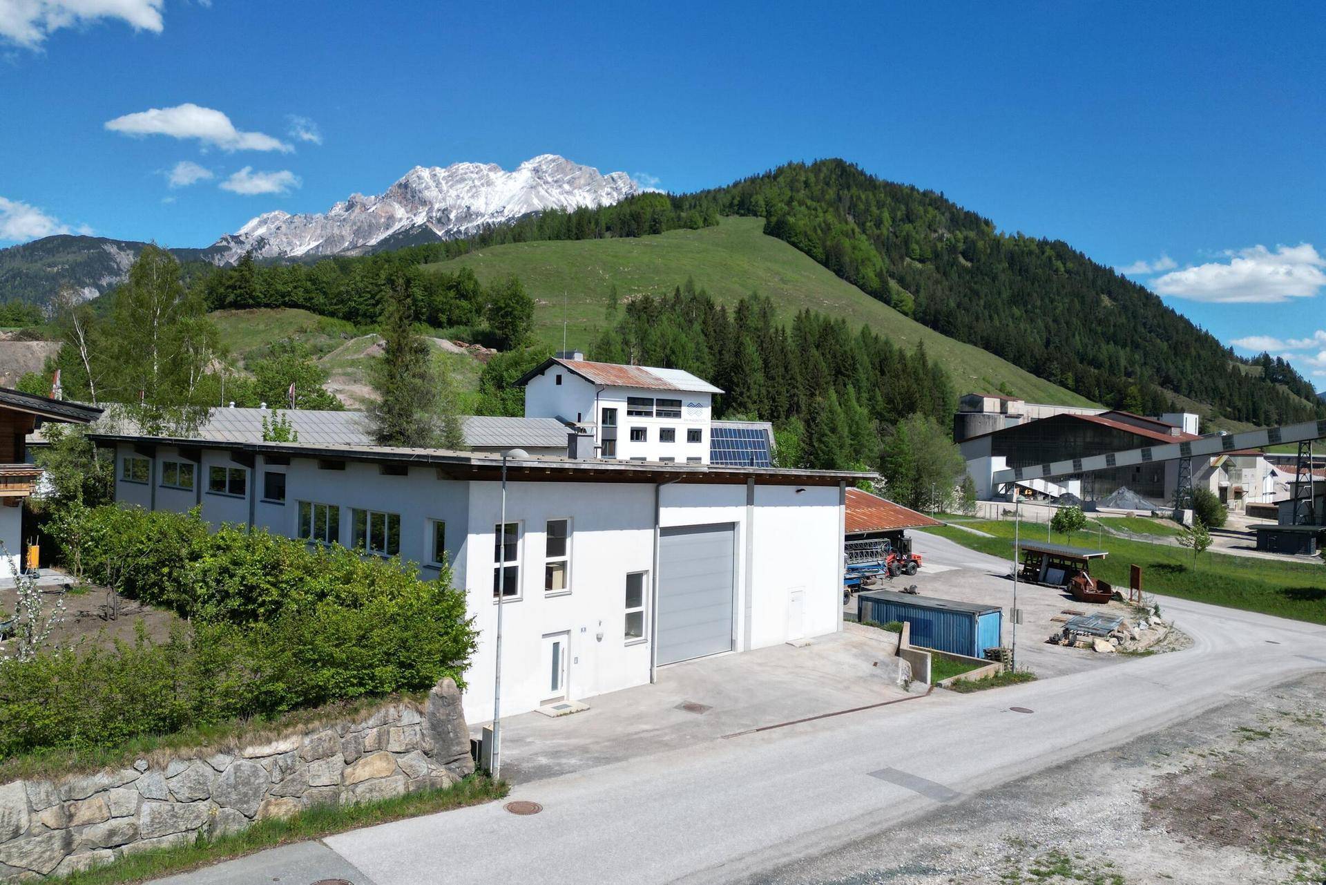 Weitläufige Außenansicht eines Gewerbegebäudes mit beeindruckender Bergkulisse und viel Grün.