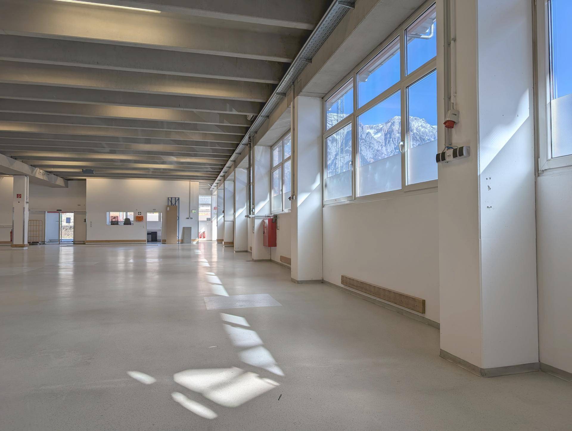 Helle Lagerhalle mit großen Fenstern, die einen Blick auf die umliegenden Berge und viel Tageslicht bieten.