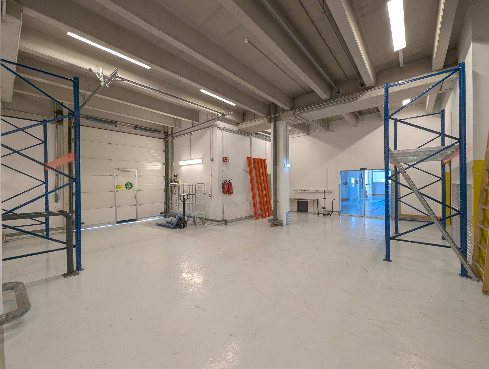 Industrielle Lagerfläche mit Rolltor, hohen Decken und Regalsystemen, bereit für den Betrieb.