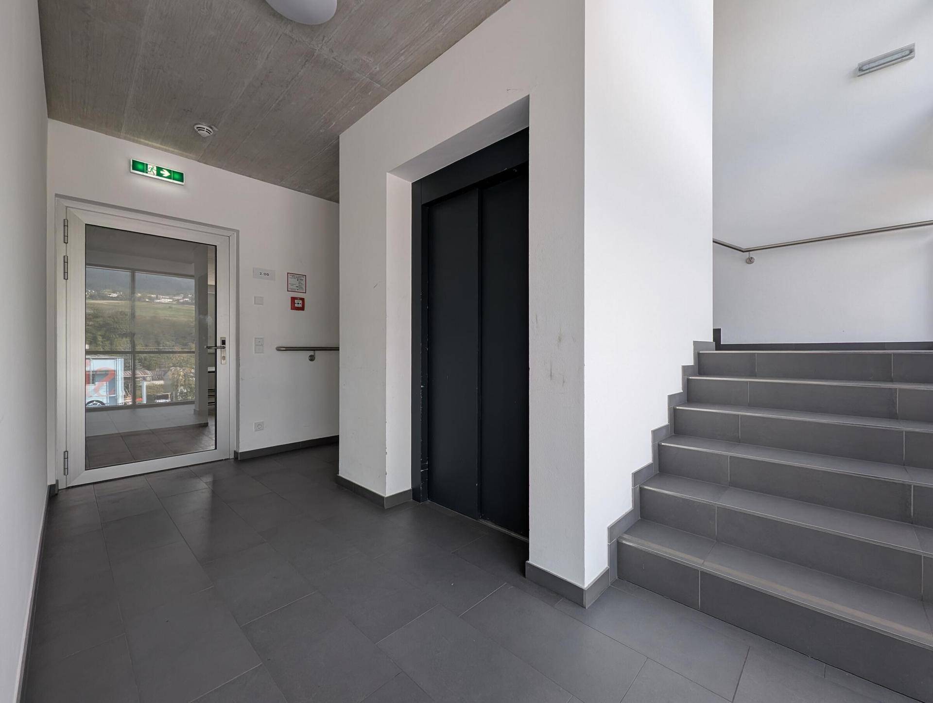 Heller Eingangsbereich mit Treppe, Aufzug und Fliesenboden, bietet Zugang zu den oberen Etagen.