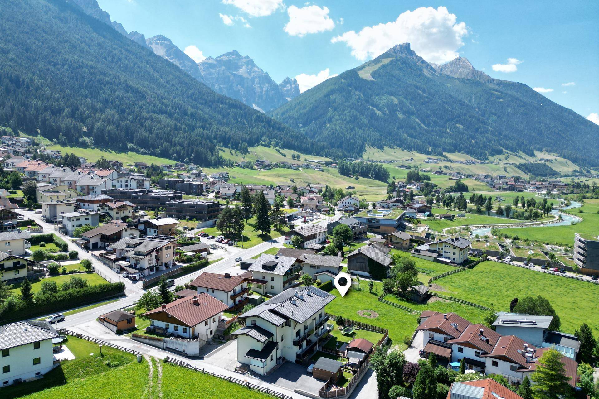 Luftaufnahme einer Siedlung in einem Tal mit grünen Wiesen und majestätischen Bergen im Hintergrund.