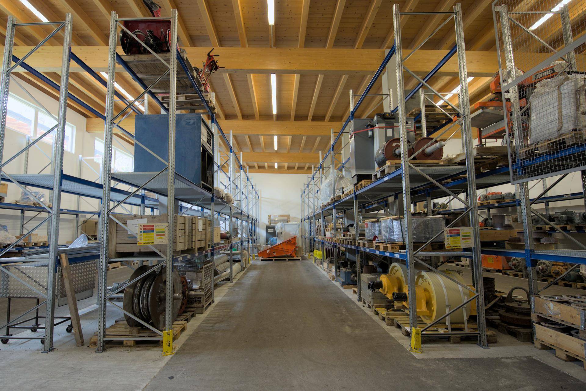 Helle Lagerhalle mit hohen Regalen, Holzbalken und Betonboden, ausgestattet für effiziente Lagerung.