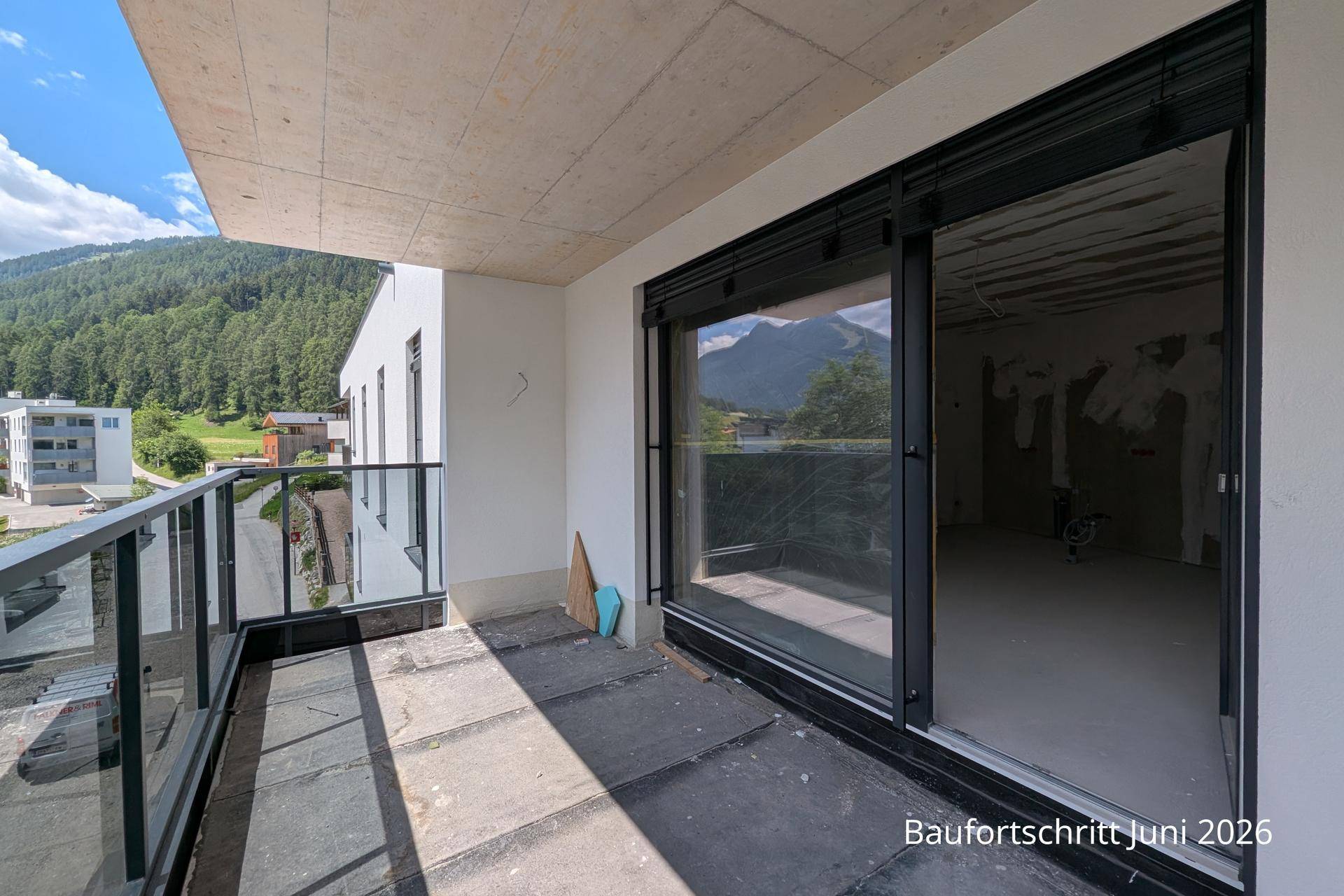 Unfertiger Innenraum mit großen Schiebetüren, die Zugang zu einem Balkon mit Bergblick bieten.