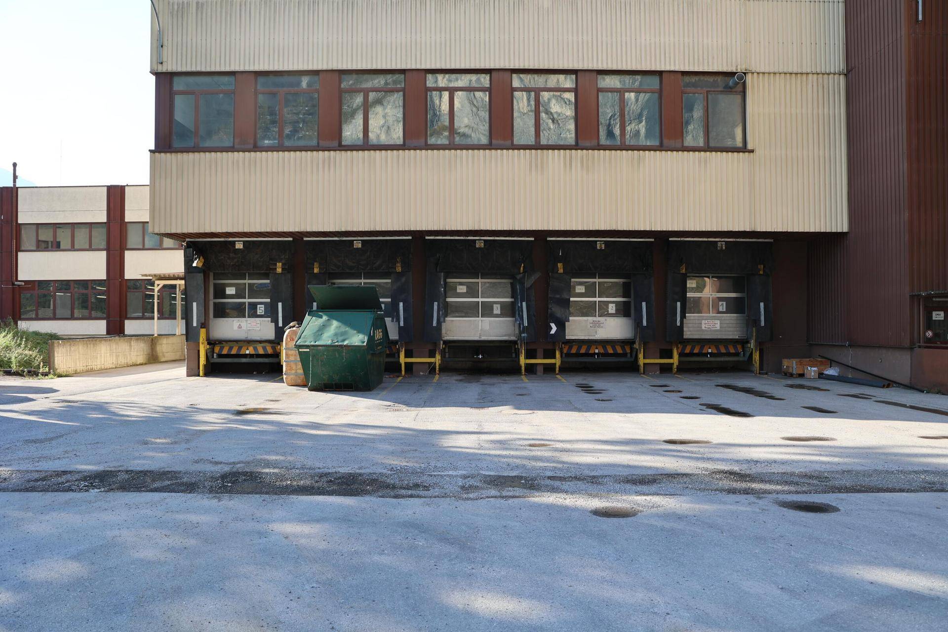 Außenansicht eines Industriegebäudes mit mehreren Laderampen und einem Müllcontainer.