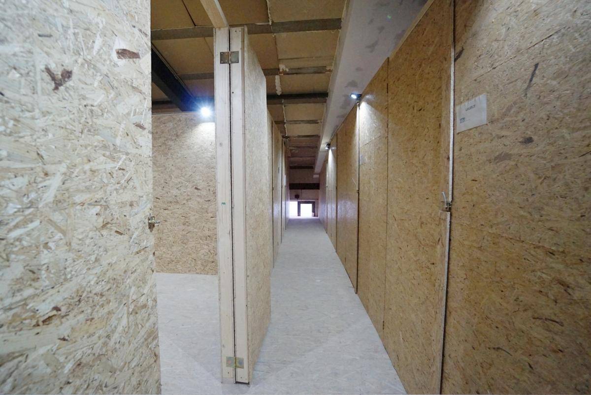 Langer, sauberer Flur mit OSB-Plattenwänden und Deckenbeleuchtung, der zu weiteren Lagereinheiten führt.