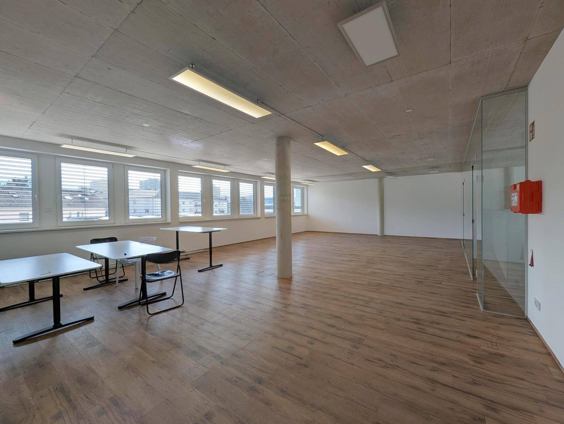 Großer, offener Büroraum mit Holzboden, Säule und vielen Fenstern, bietet flexible Gestaltungsmöglichkeiten.